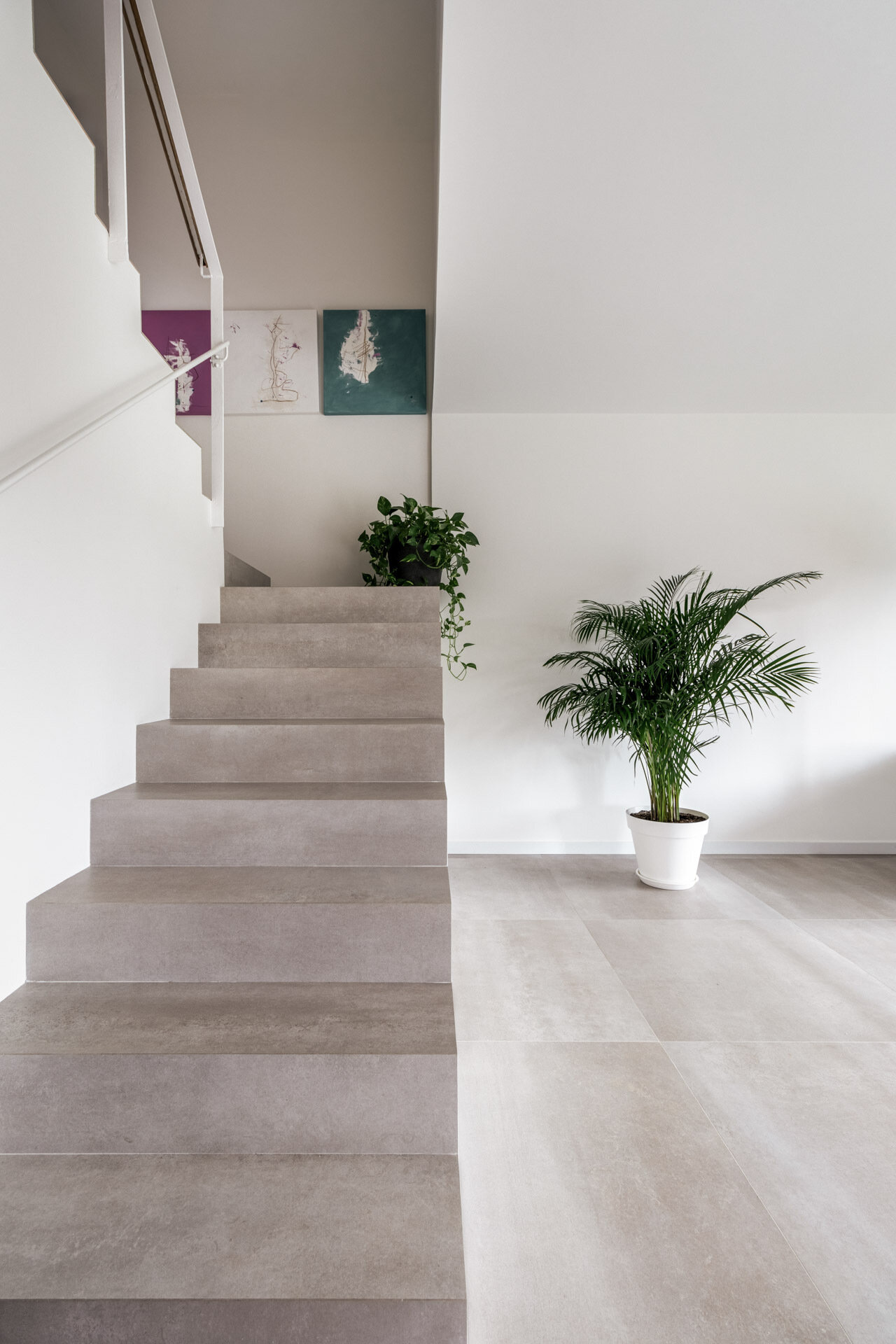 The original staircase remains in D + A House as a solid light-grey volume, joined by an exposed concrete column that preserves part of the home's original structure.