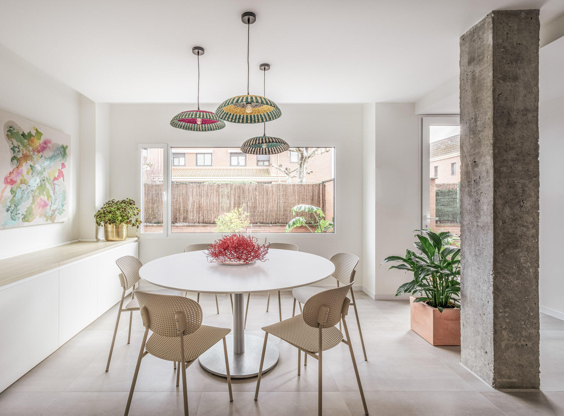 A round white dining table, perforated chairs and natural-fibre pendant lights create an informal dining area near the entrance of this Madrid home.