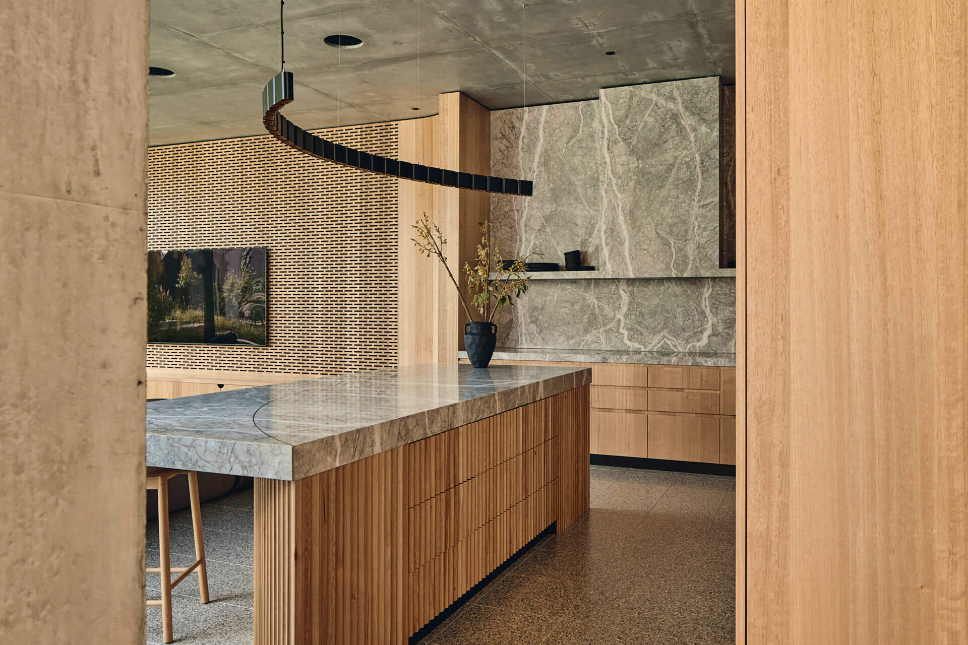 Babylonia's unusual T-shaped kitchen combines timber and stone within the open-plan living area, with the Melbourne home's rising garden visible beyond.