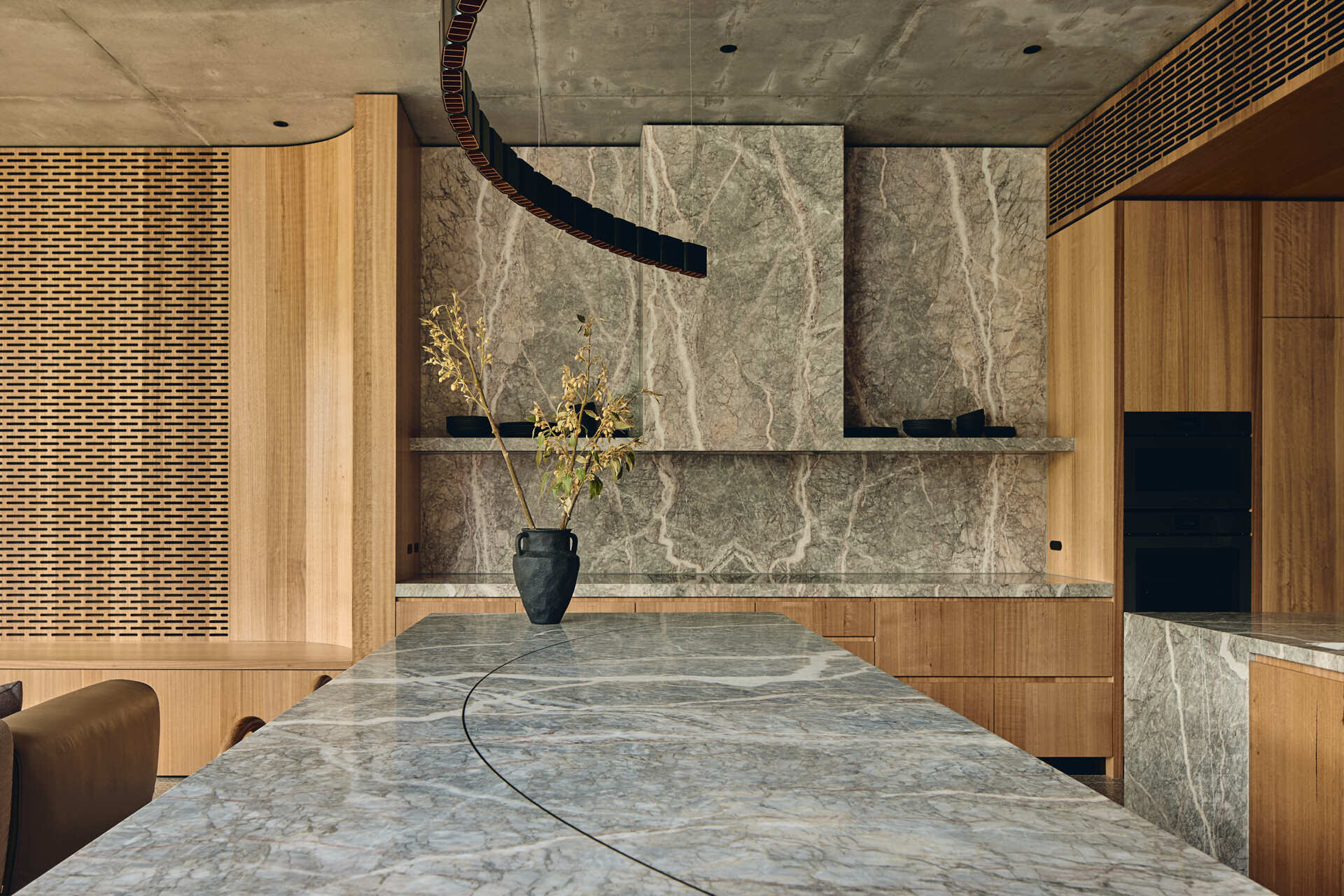 Babylonia's unusual T-shaped kitchen combines timber and stone within the open-plan living area, with the Melbourne home's rising garden visible beyond.
