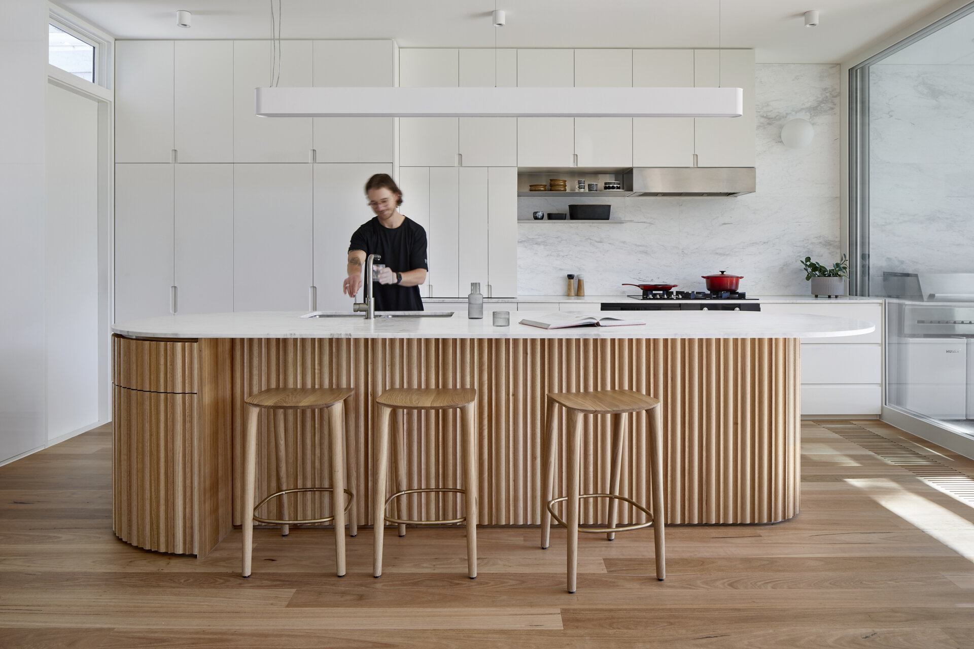 A generous Melbourne kitchen combines Blackbutt timber and white cabinets, with a island that adds texture and curves.