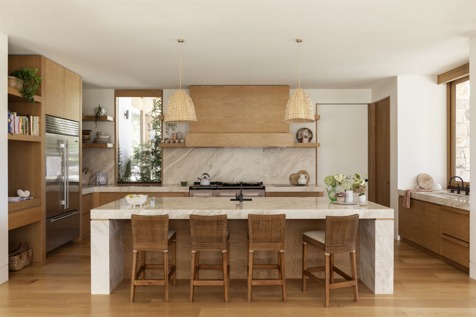 Natural wood cabinetry, woven pendant lights and softly veined stone give the kitchen and pantry a warm, relaxed character while keeping the look clean and contemporary. The oversized island provides plenty of space for cooking, casual meals and gathering with friends, with woven counter stools adding comfort and texture.