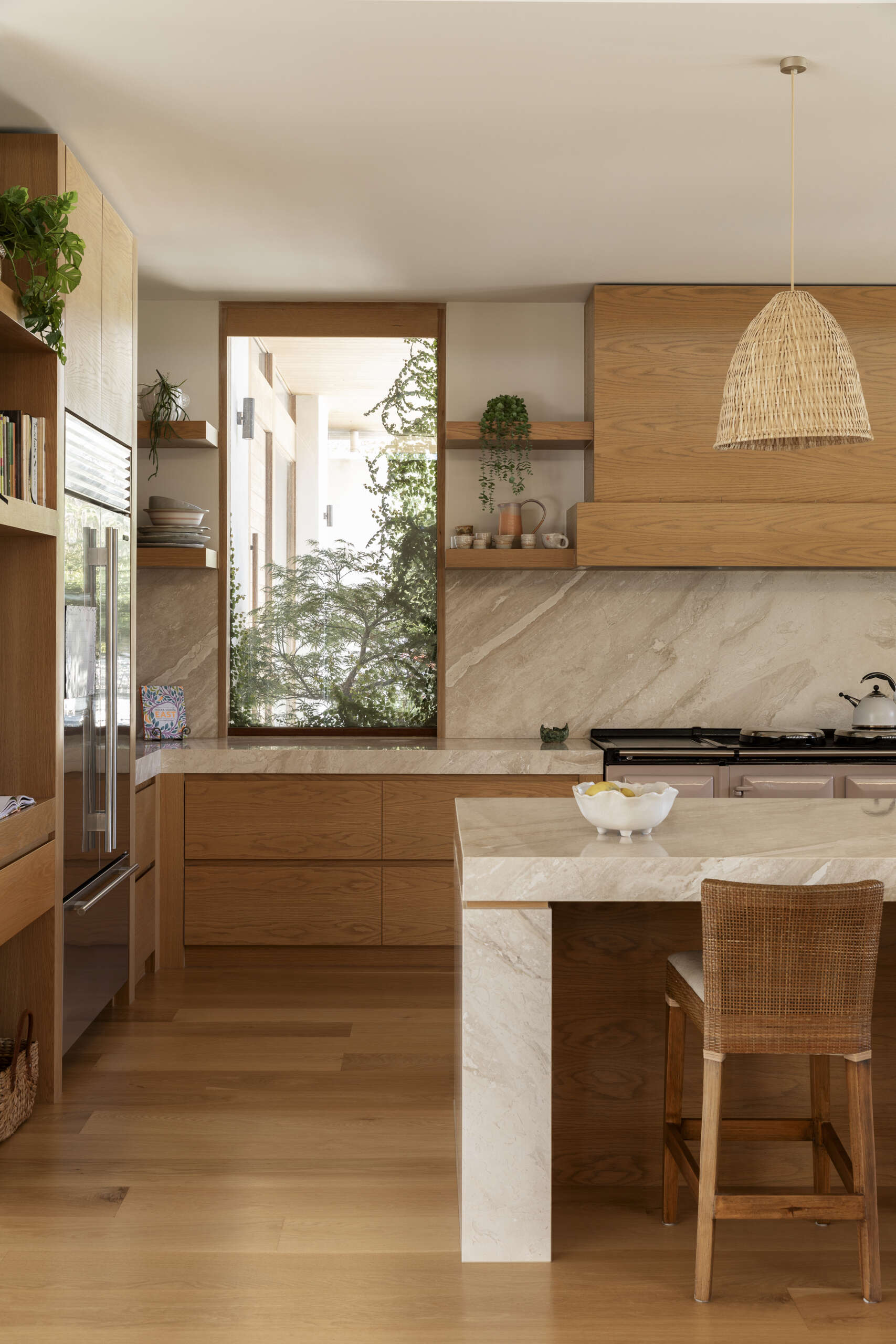 Natural wood cabinetry, woven pendant lights and softly veined stone give the kitchen and pantry a warm, relaxed character while keeping the look clean and contemporary. The oversized island provides plenty of space for cooking, casual meals and gathering with friends, with woven counter stools adding comfort and texture.