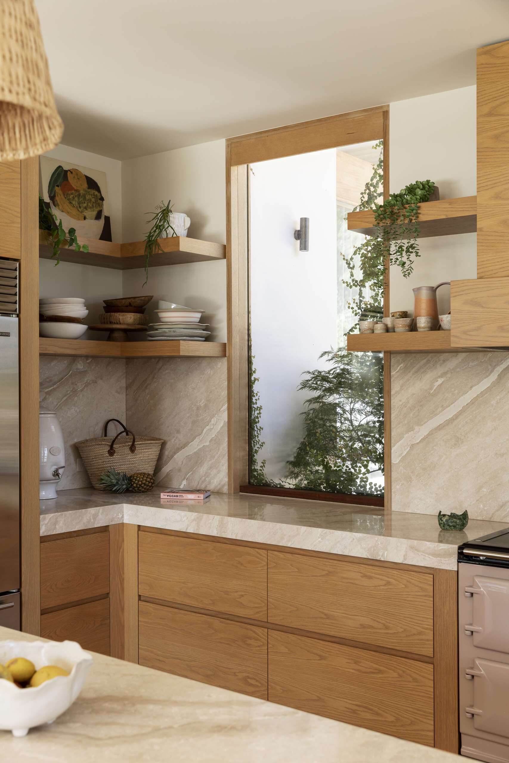 Natural wood cabinetry, woven pendant lights and softly veined stone give the kitchen and pantry a warm, relaxed character while keeping the look clean and contemporary. The oversized island provides plenty of space for cooking, casual meals and gathering with friends, with woven counter stools adding comfort and texture.
