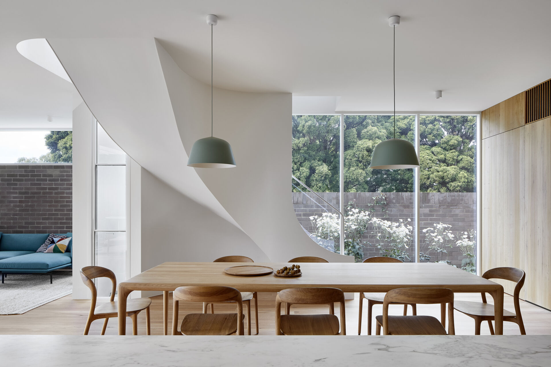 The dining area flows directly from the kitchen, with warm Blackbutt floors, white walls, and curved furniture.