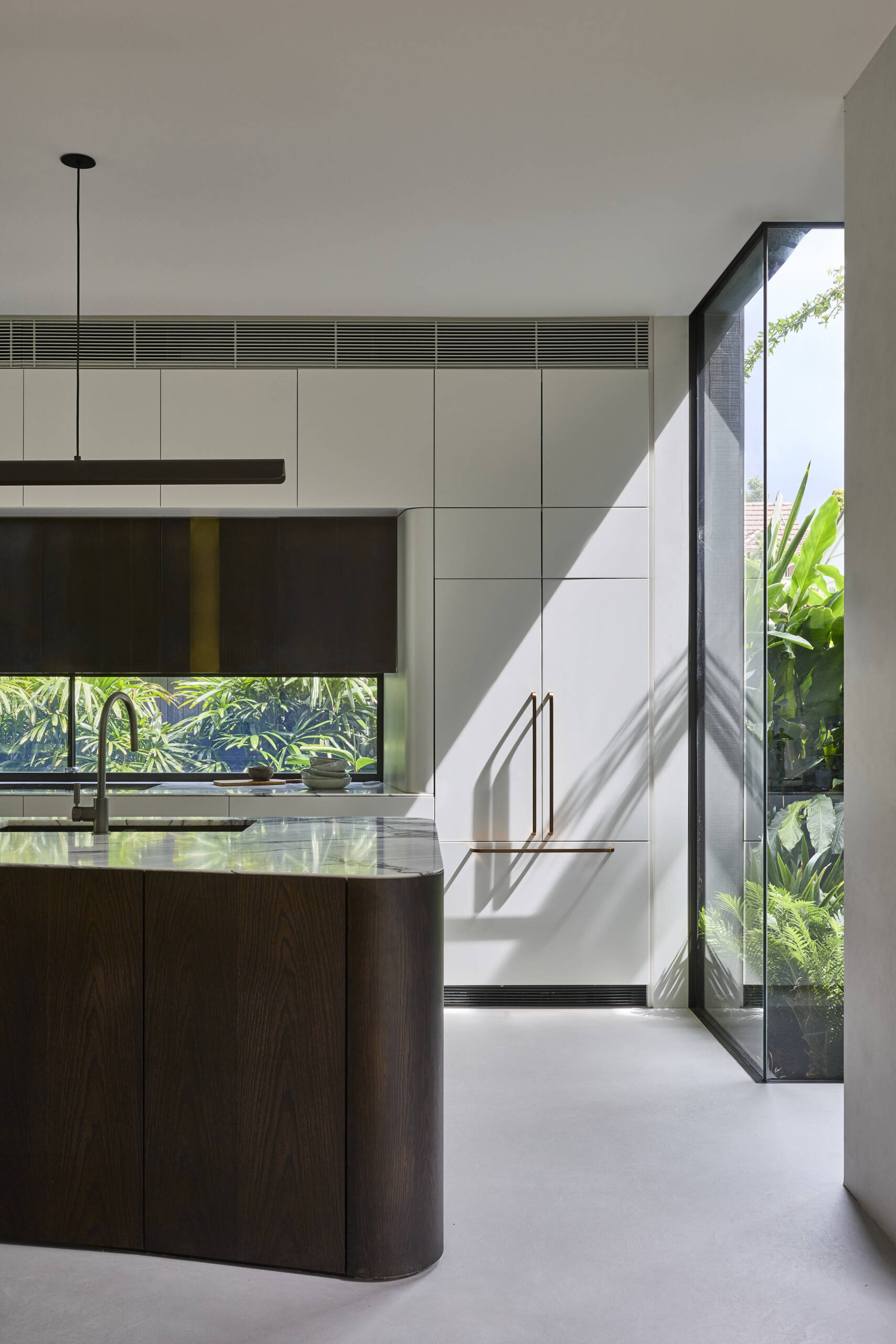 Tour the contemporary kitchen at Sasso Nero, where dark oak, pale stone and crisp white cabinetry create a refined contrast. Garden views, bronze-toned details and a slim linear pendant complete the space.