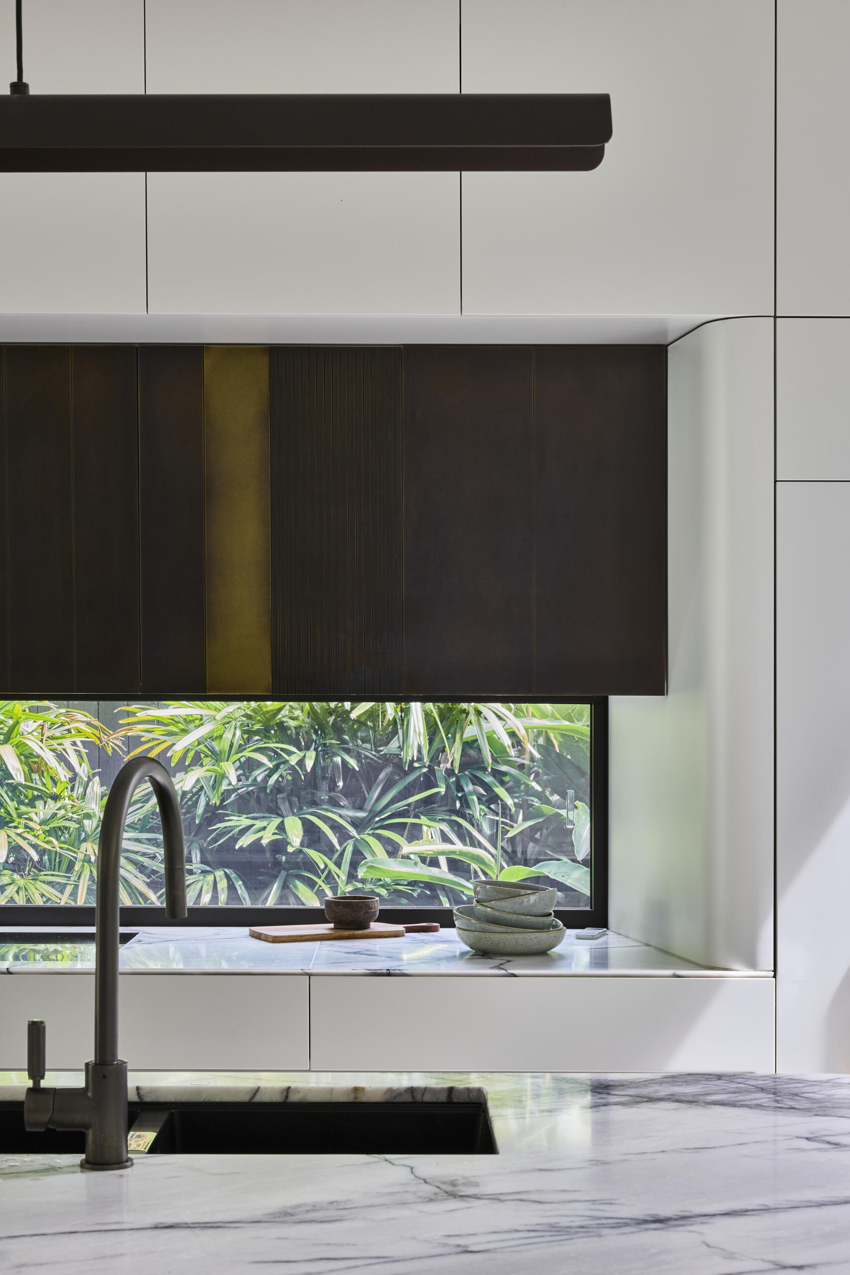 Tour the contemporary kitchen at Sasso Nero, where dark oak, pale stone and crisp white cabinetry create a refined contrast. Garden views, bronze-toned details and a slim linear pendant complete the space.
