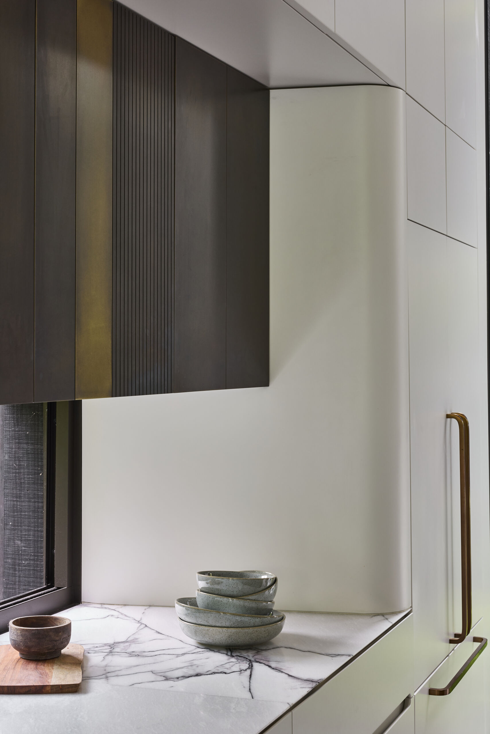 Tour the contemporary kitchen at Sasso Nero, where dark oak, pale stone and crisp white cabinetry create a refined contrast. Garden views, bronze-toned details and a slim linear pendant complete the space.