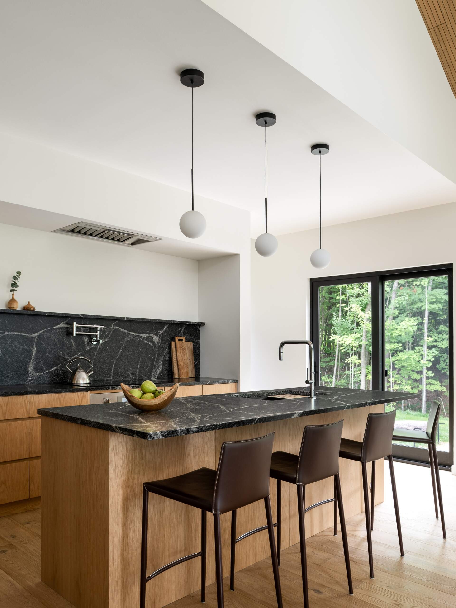 Explore the dining and kitchen spaces of this Vermont hillside home, featuring lofty ceilings, lighter wood finishes, natural light and views through the surrounding trees.
