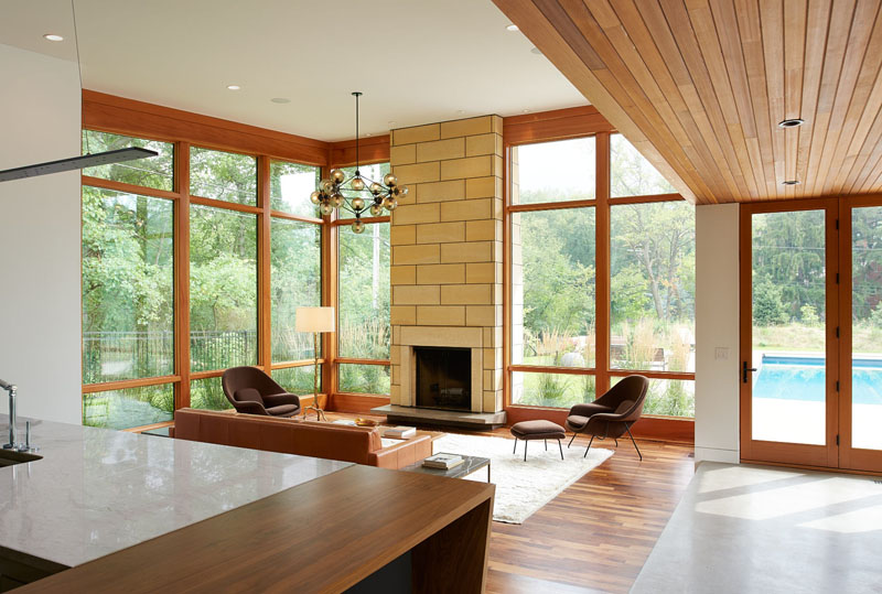 A warm modern living room in a Minneapolis ranch house, featuring a limestone fireplace surround, wood-framed windows and plenty of natural light overlooking the surrounding landscape.