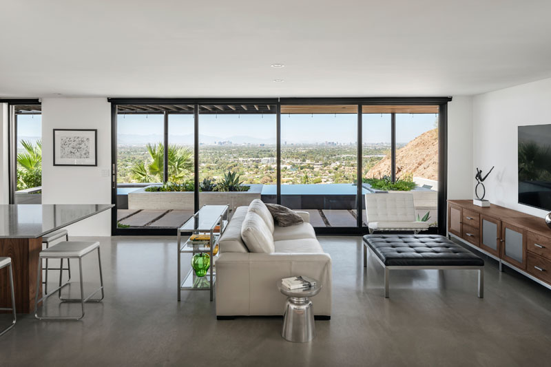 Floor-to-ceiling windows and sliding glass doors open the Red Rocks residence toward Camelback Mountain. Concrete floors, walnut cabinetry, white cabinetry and stone surfaces create a simple contemporary interior.