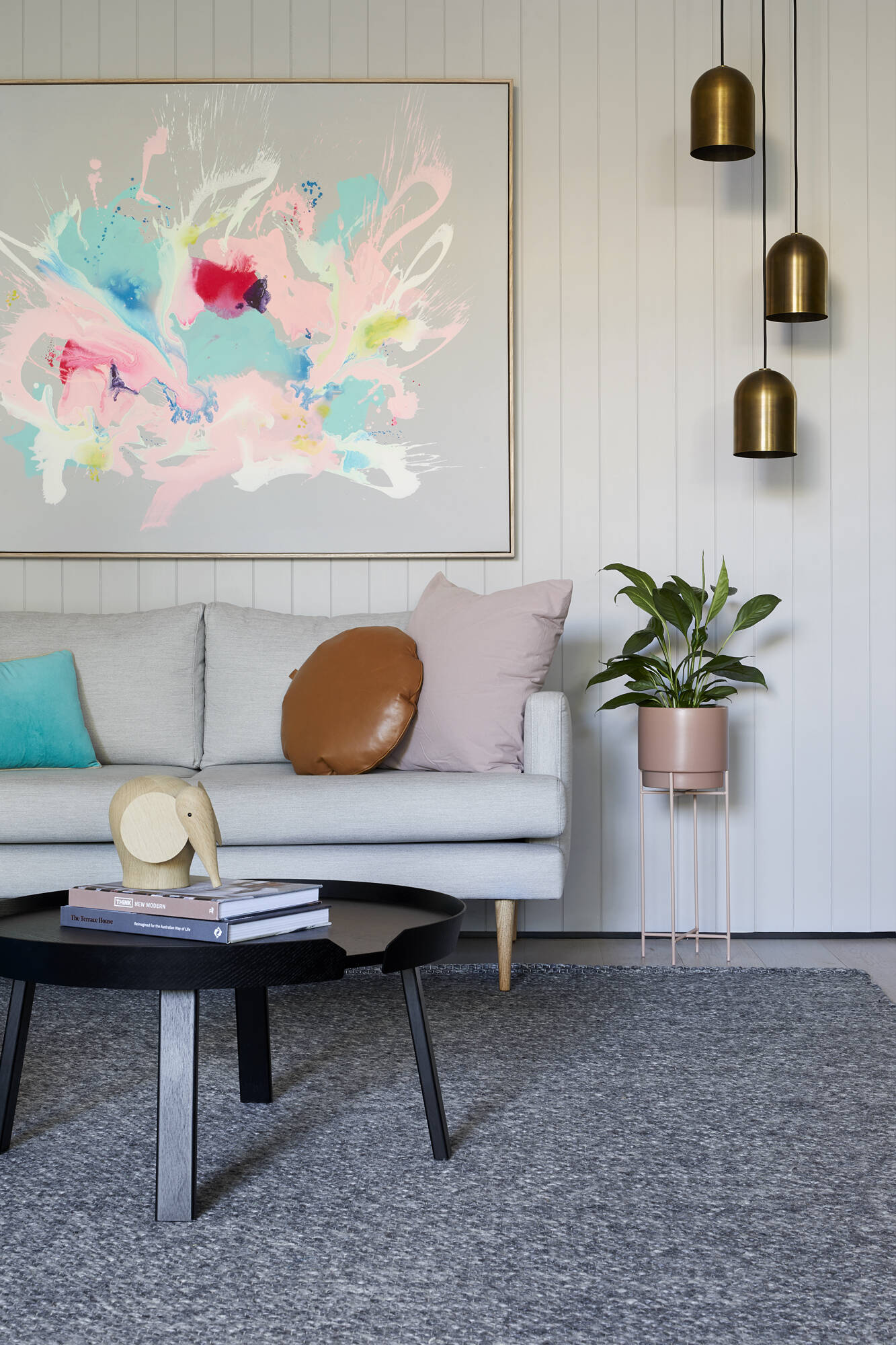White walls, colorful abstract art, metallic pendant lights, and indoor plants give this modern Australian living room plenty of personality.