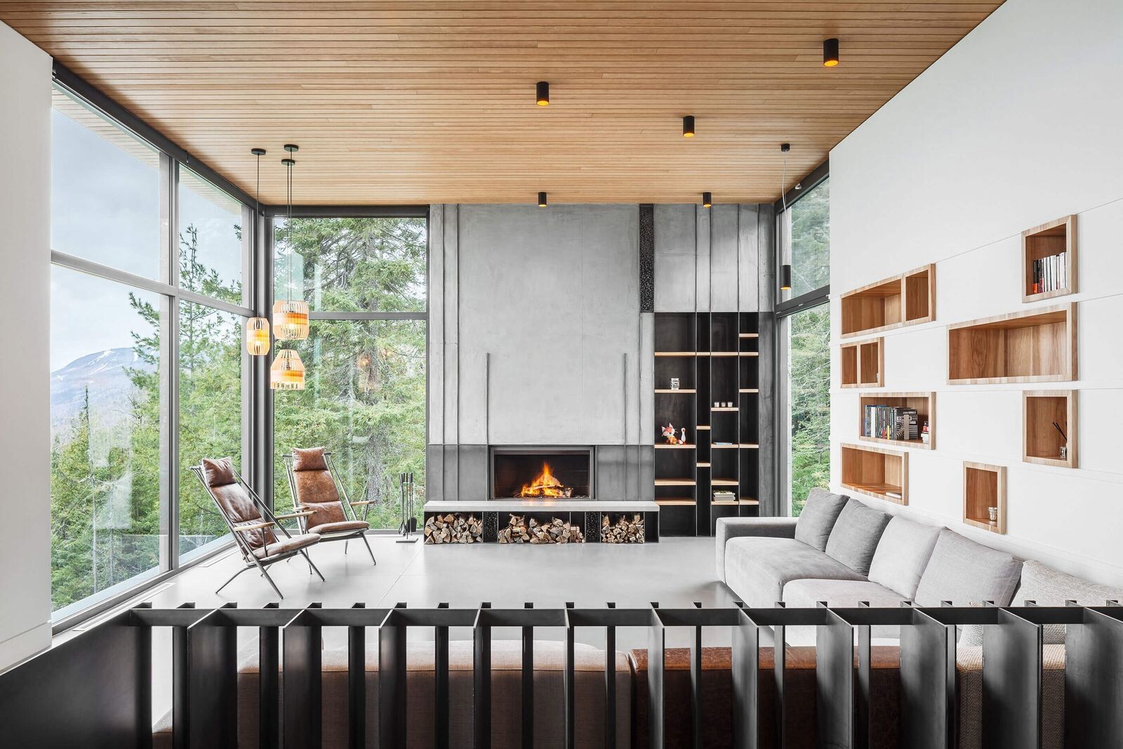 Explore the living room of Long Horizontals, where wood-lined shelving, a concrete fireplace and an open floor plan create a warm contemporary interior.