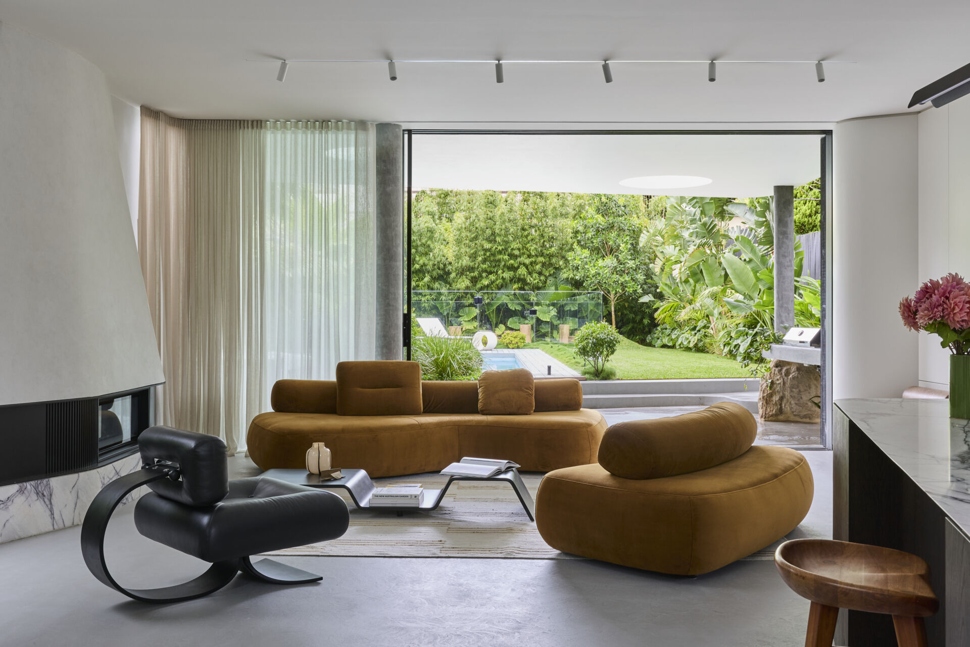 Inside Sasso Nero's living room, dark heavily grained oak, natural stone and bronze details create a rich material palette. An Oscar Niemeyer Alta lounge chair adds a sculptural design element beside the fireplace.