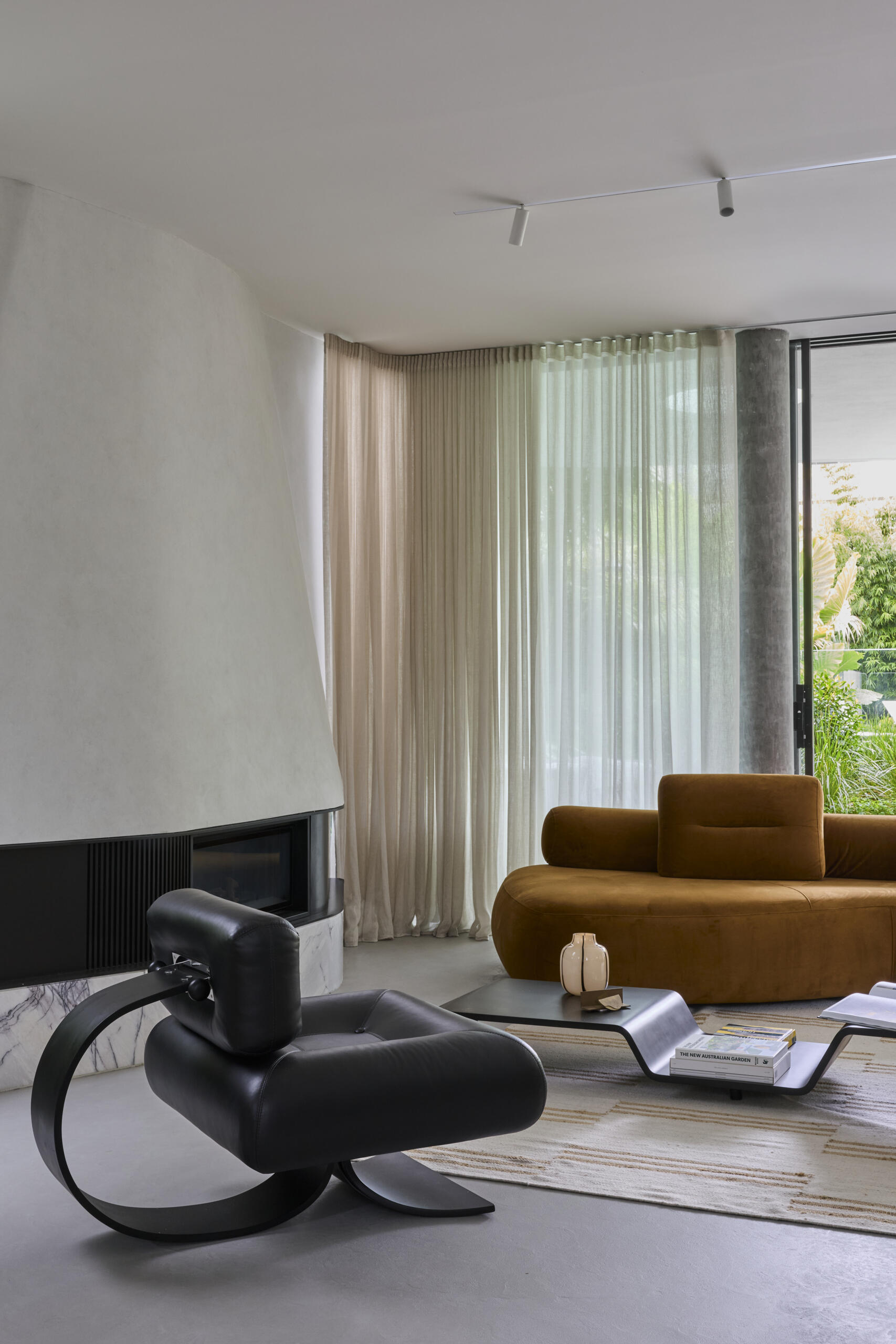 Inside Sasso Nero's living room, dark heavily grained oak, natural stone and bronze details create a rich material palette. An Oscar Niemeyer Alta lounge chair adds a sculptural design element beside the fireplace.