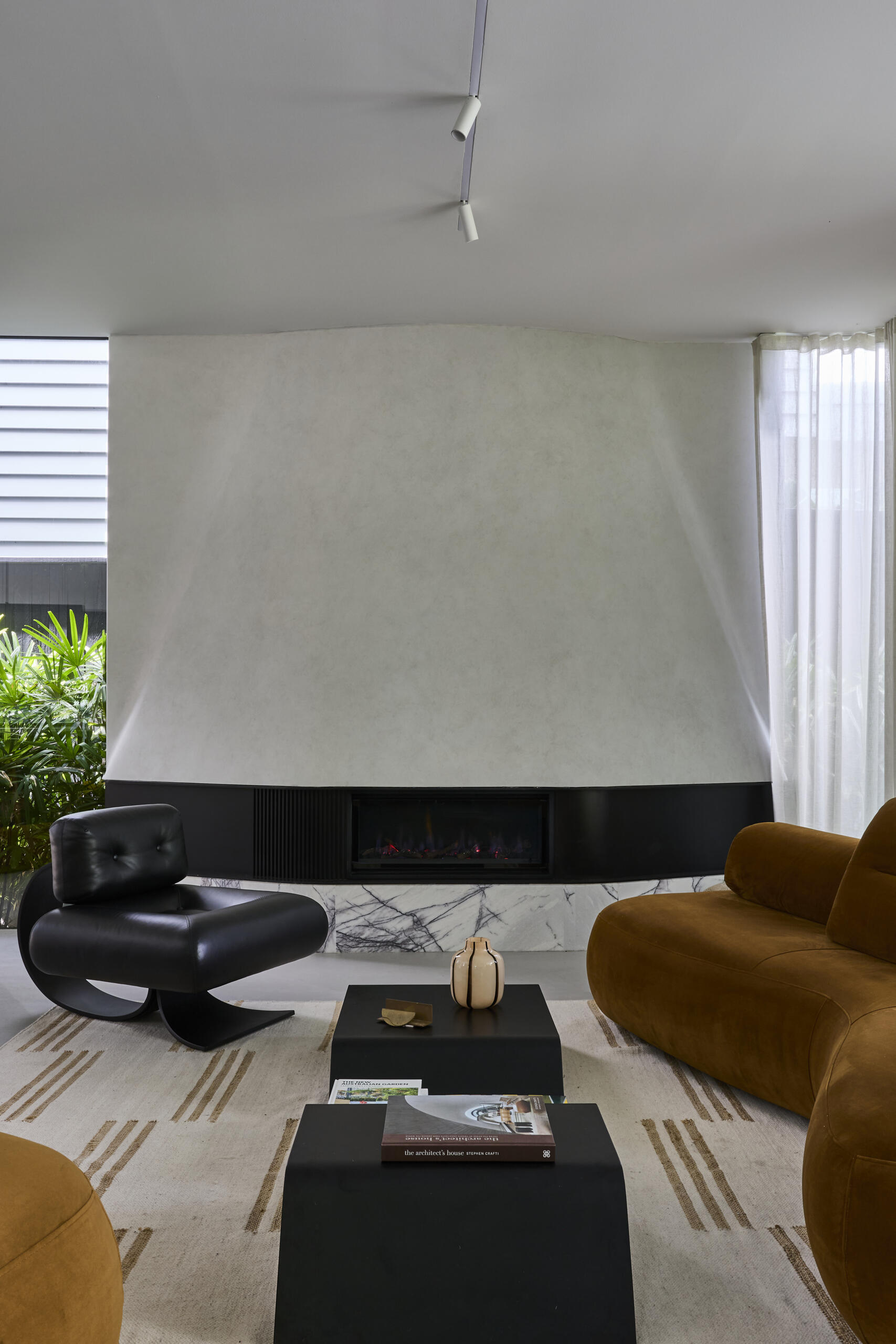 Inside Sasso Nero's living room, dark heavily grained oak, natural stone and bronze details create a rich material palette. An Oscar Niemeyer Alta lounge chair adds a sculptural design element beside the fireplace.