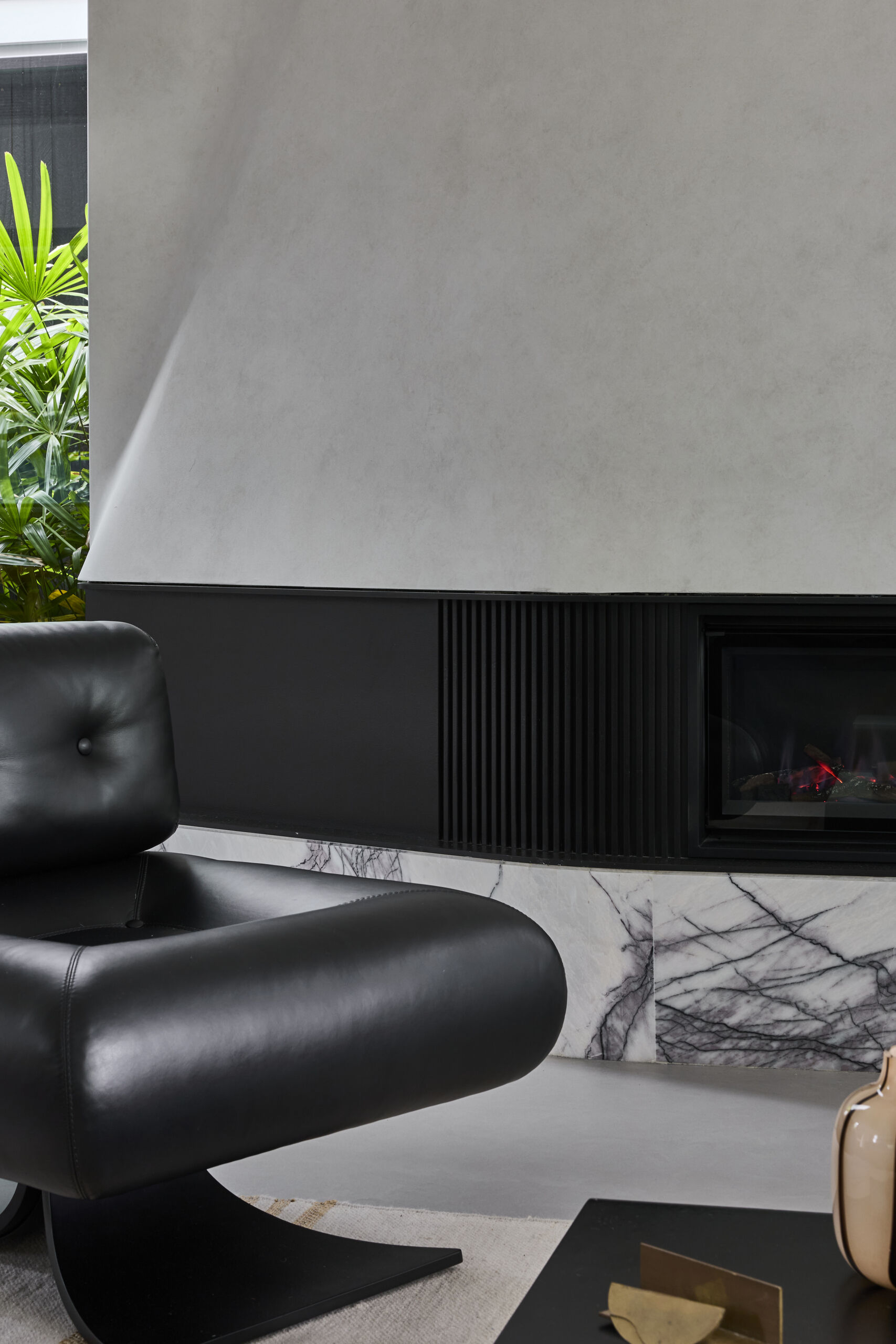 Inside Sasso Nero's living room, dark heavily grained oak, natural stone and bronze details create a rich material palette. An Oscar Niemeyer Alta lounge chair adds a sculptural design element beside the fireplace.