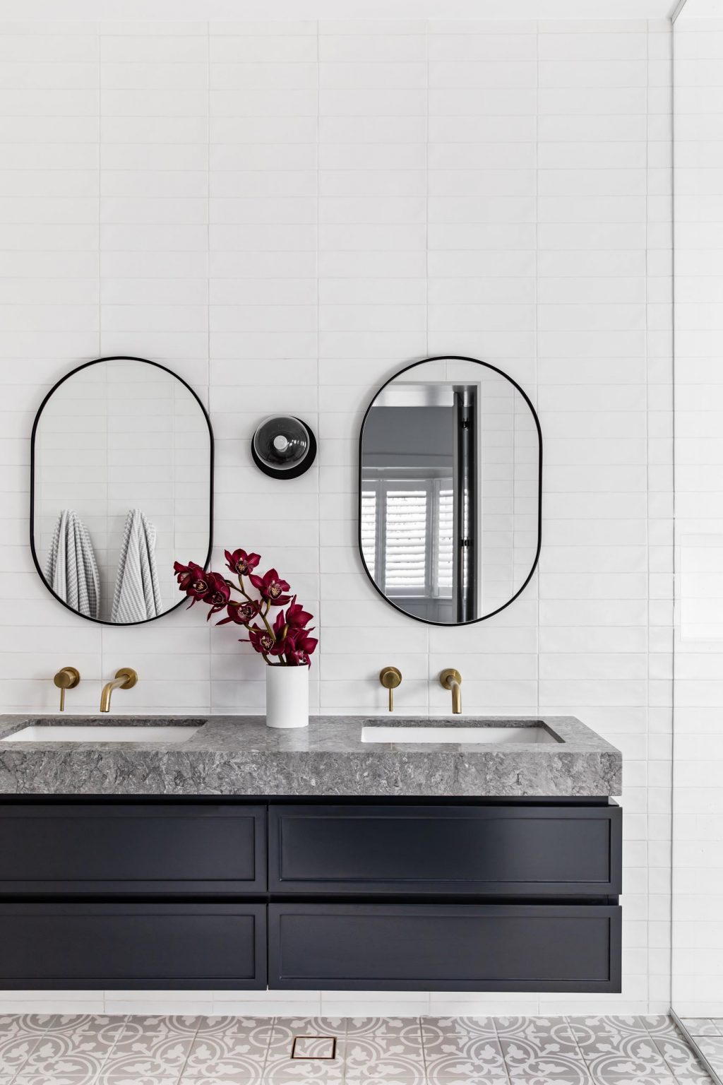 Tour the hidden ensuite behind the custom wardrobe doors, featuring patterned floor tiles, a black floating vanity, grey stone, white subway tiles, brass hardware and a double shower.