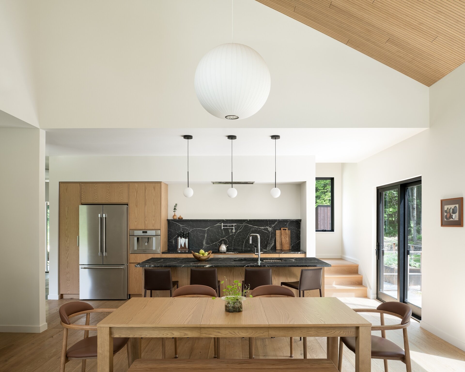 Explore the dining and kitchen spaces of this Vermont hillside home, featuring lofty ceilings, lighter wood finishes, natural light and views through the surrounding trees.