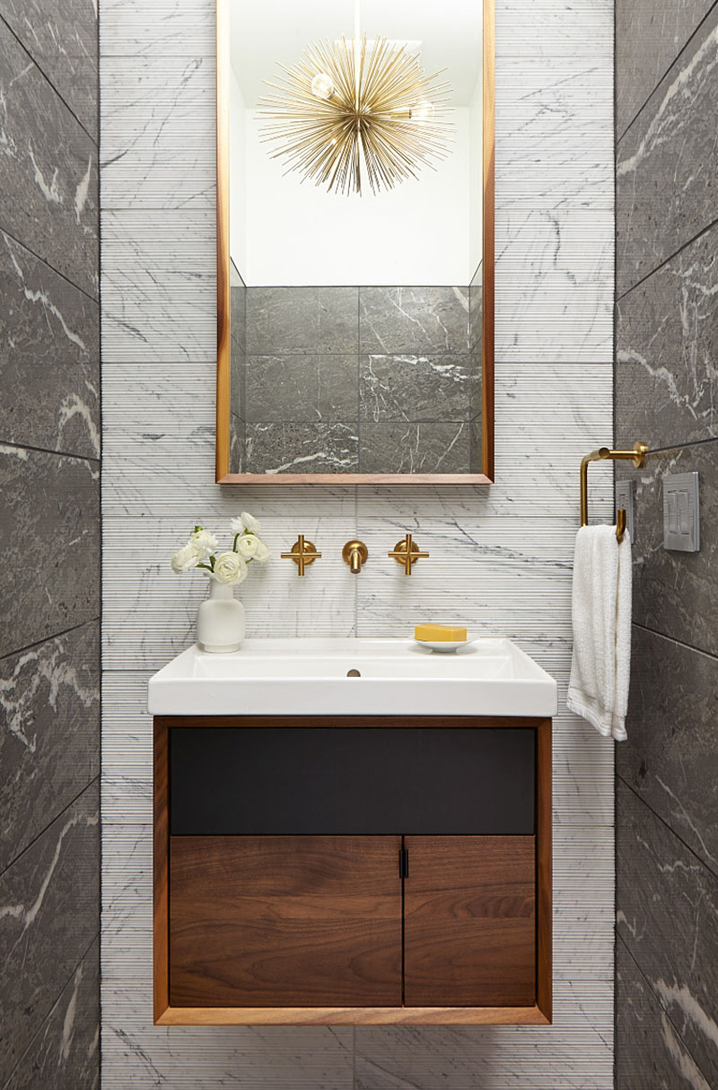 Brass accents and a tall mirror brighten the compact powder room of this modern Minneapolis ranch house by Strand Design.