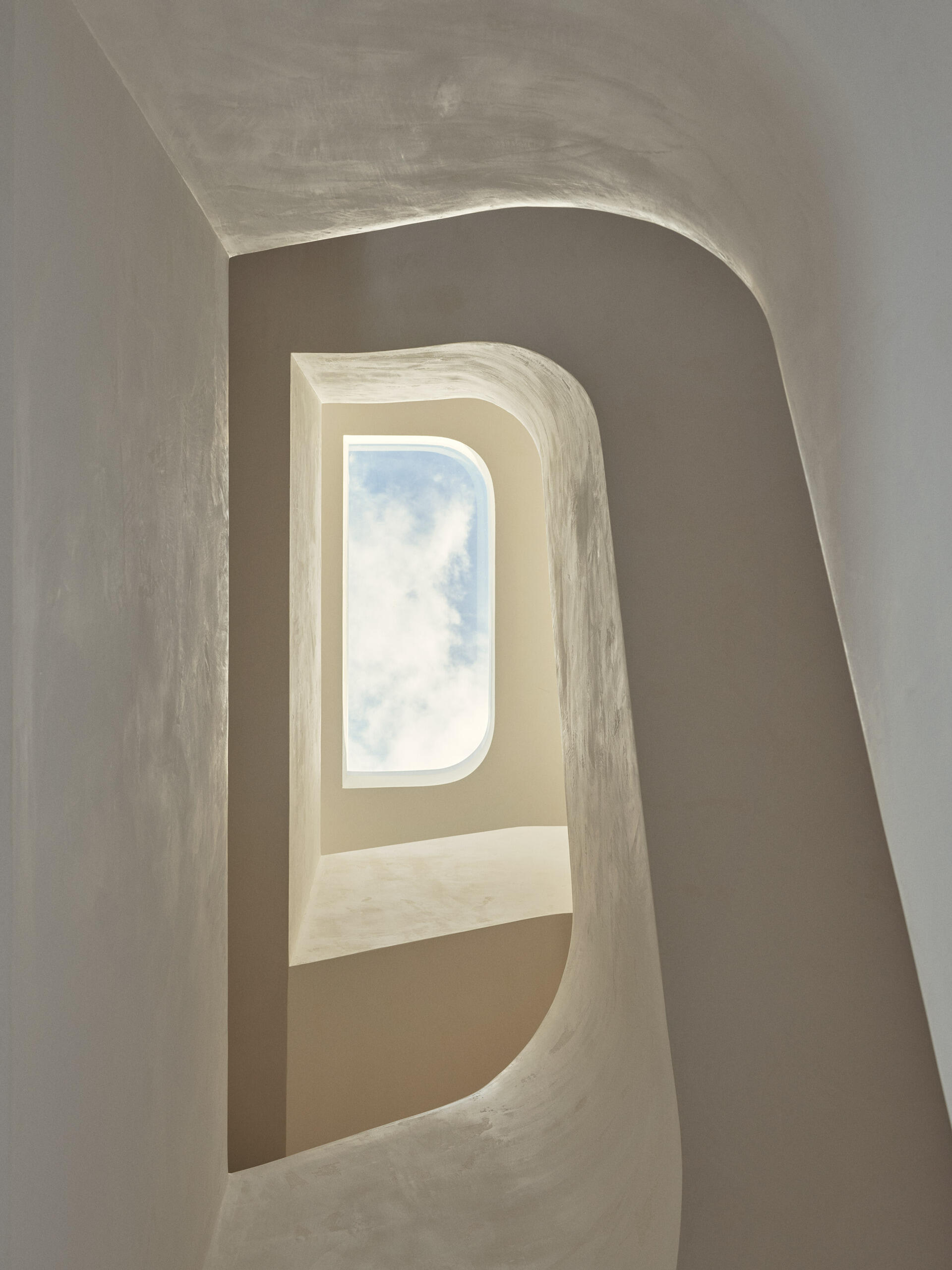 A sculptural helical staircase ribbons through the centre of this Byron Bay home, connecting the upper levels beneath a large skylight that brings natural light into the heart of the house.