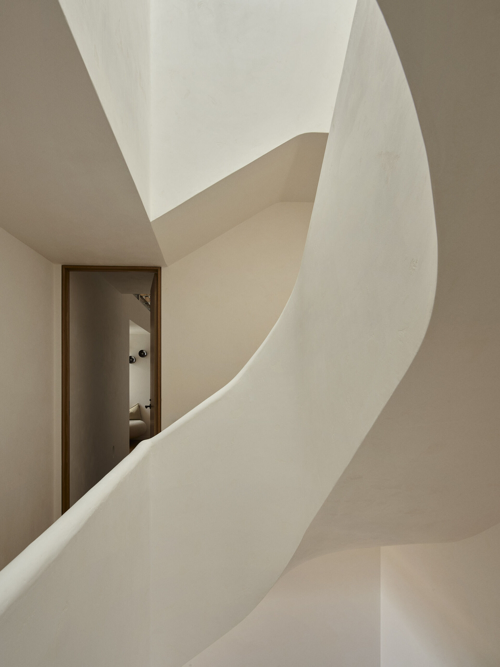 A sculptural helical staircase ribbons through the centre of this Byron Bay home, connecting the upper levels beneath a large skylight that brings natural light into the heart of the house.