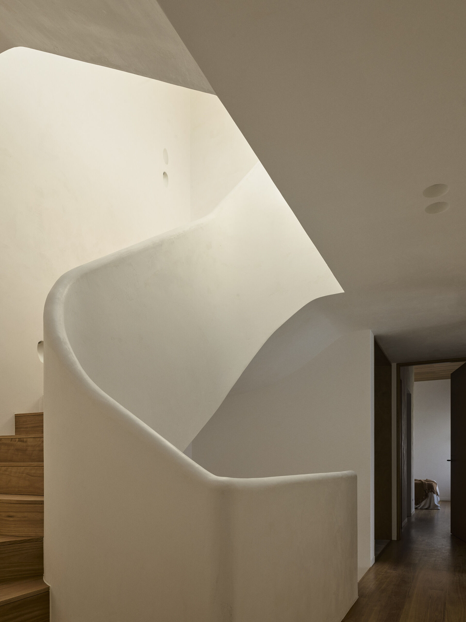 A sculptural helical staircase ribbons through the centre of this Byron Bay home, connecting the upper levels beneath a large skylight that brings natural light into the heart of the house.