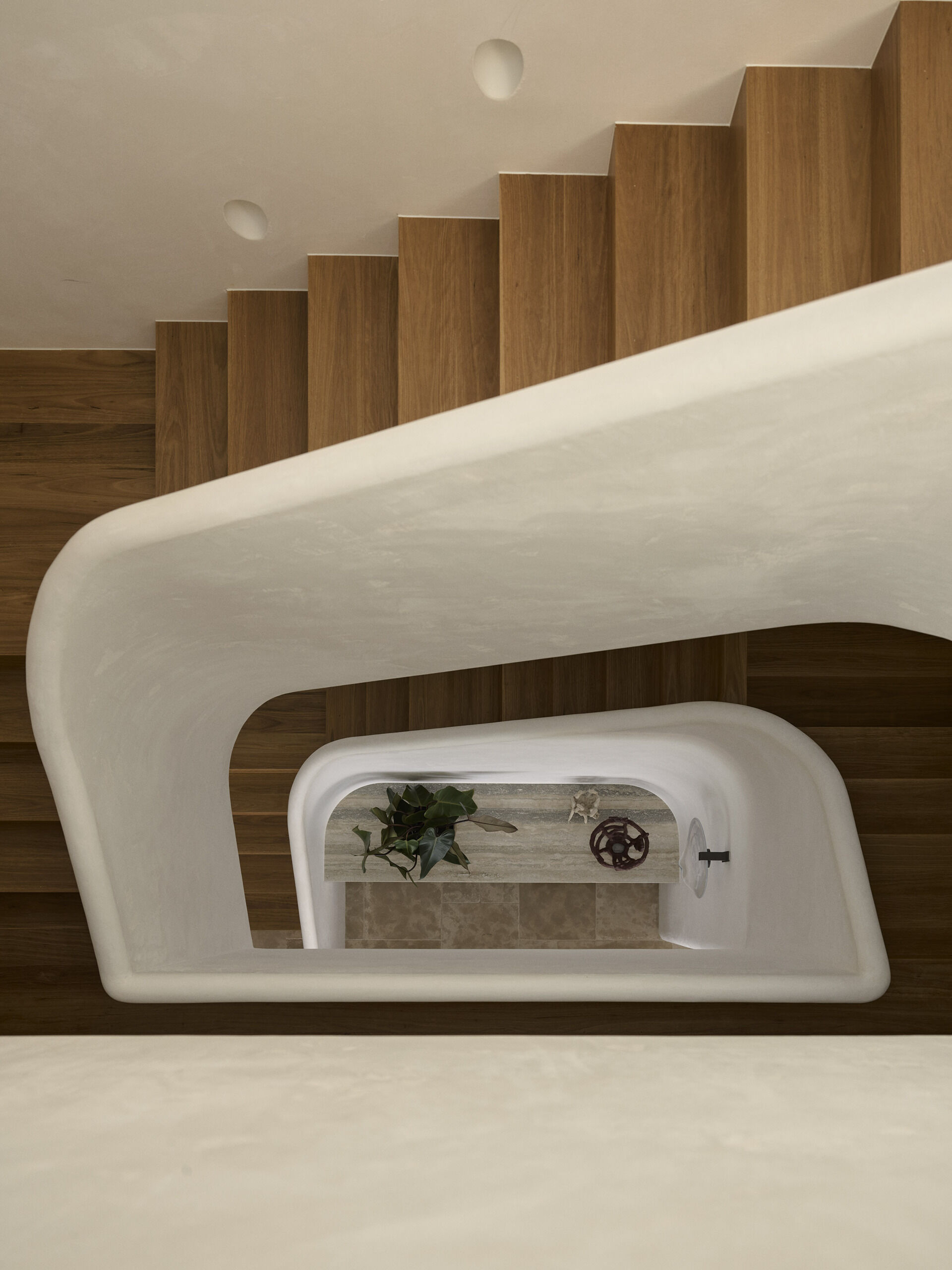 A sculptural helical staircase ribbons through the centre of this Byron Bay home, connecting the upper levels beneath a large skylight that brings natural light into the heart of the house.
