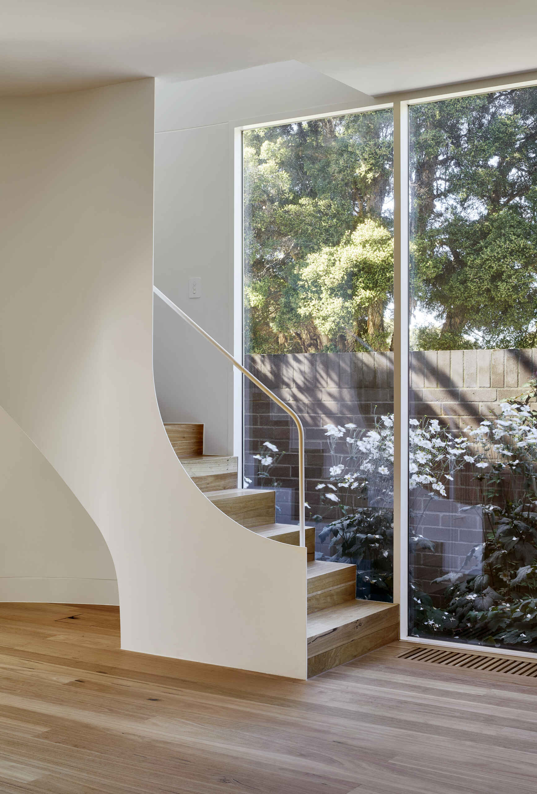 A curved staircase arcs through the living and dining area, continuing the soft architectural language of the extension, while a discreet lift improves accessibility between floors.