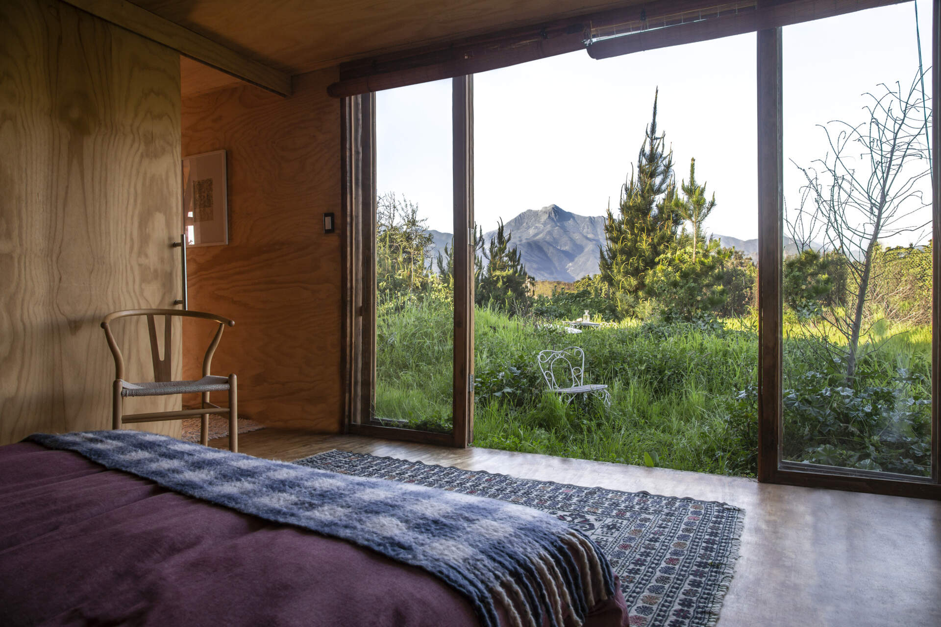 The bedroom in this tiny house is positioned to capture the surrounding landscape. Sliding glass doors open to offers an uninterrupted outlook toward the grove of mature quillay and molle trees that first inspired the project.