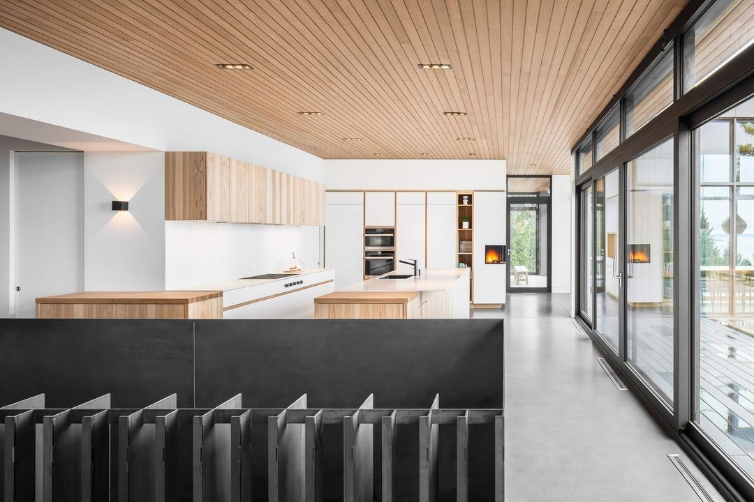 Light wood and white cabinetry give the kitchen of this Québec house a clean contemporary look, while floor-to-ceiling windows bring natural light into the space.
