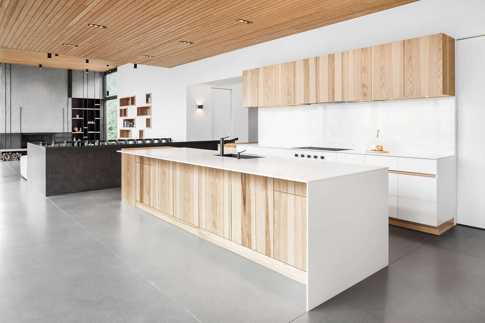 Light wood and white cabinetry give the kitchen of this Québec house a clean contemporary look, while floor-to-ceiling windows bring natural light into the space.