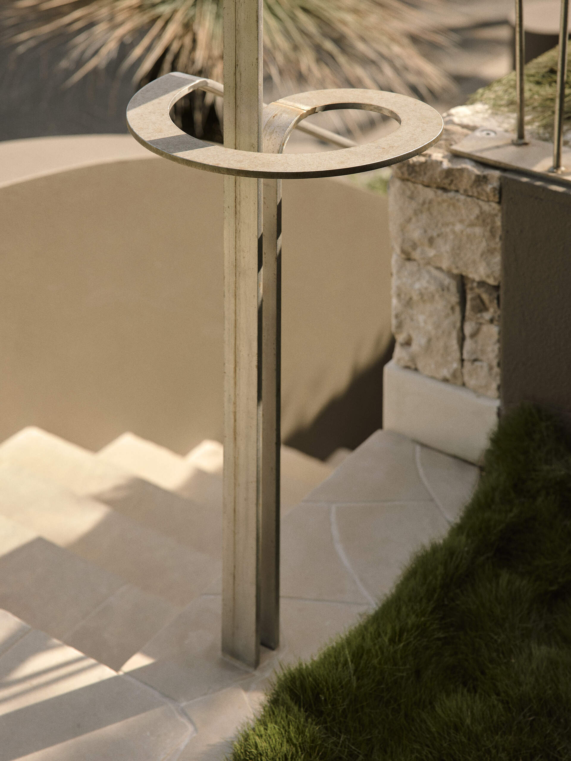 Curved taupe stucco walls, pale stone steps and lush planting create a sculptural entrance to this Byron Bay home, softened by a mature grass tree and touches of purple flowers.