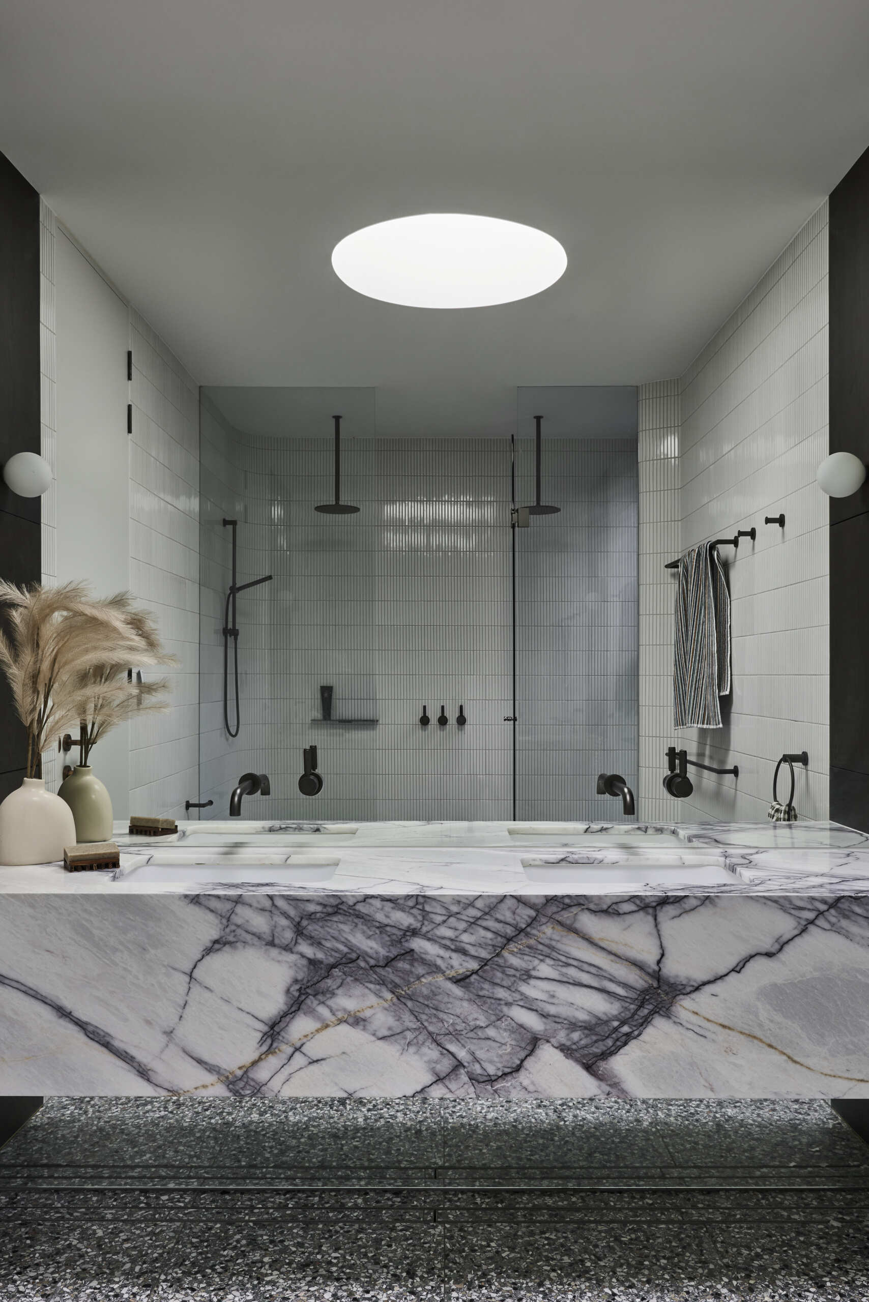 Explore the primary bathroom at Sasso Nero, where a marble double vanity with bold grey veining meets white wall tiles, matte black fixtures and a large overhead skylight.