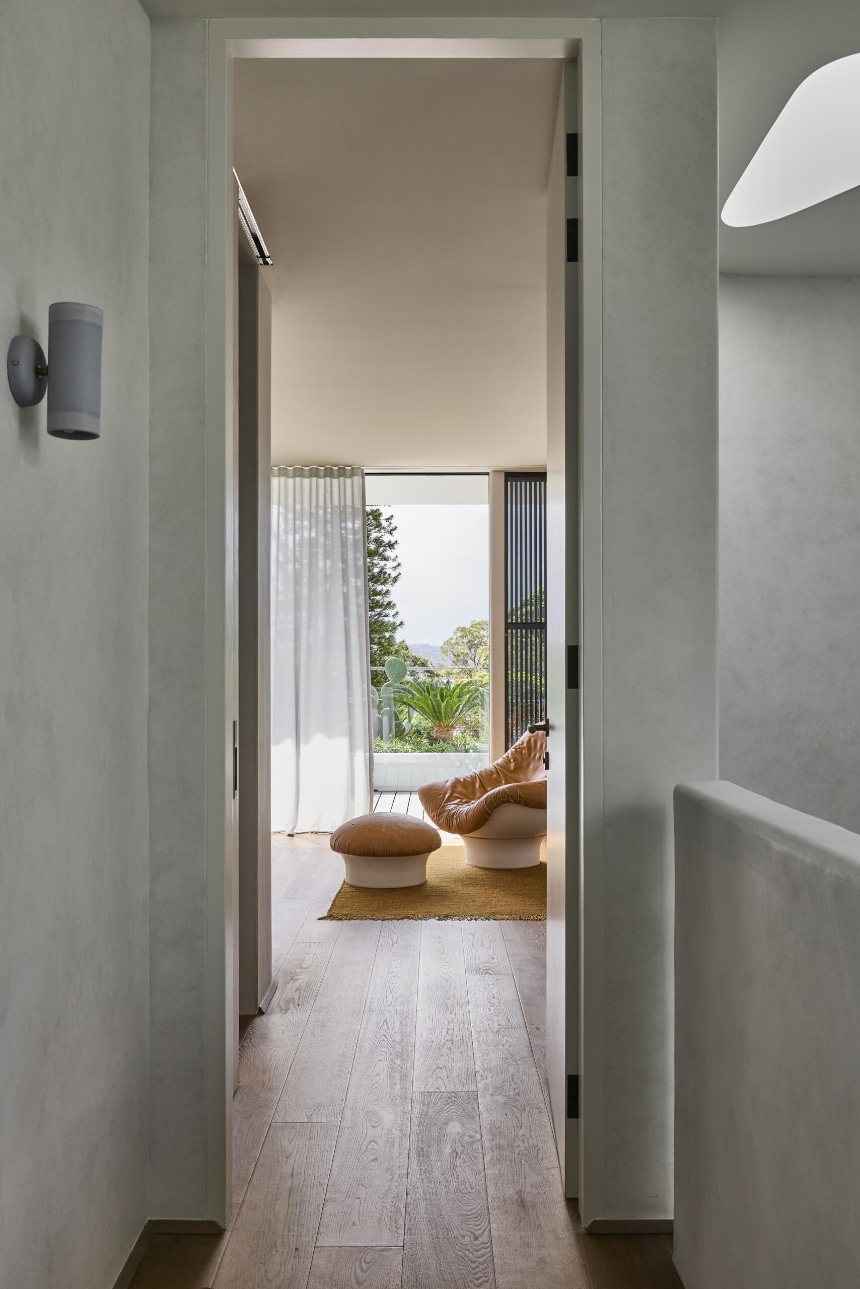 Step inside the primary bedroom at Sasso Nero, featuring a softly curved plaster wall, dark timber headboard, neutral bedding and warm wood floors. The restrained palette creates a calm contemporary interior.