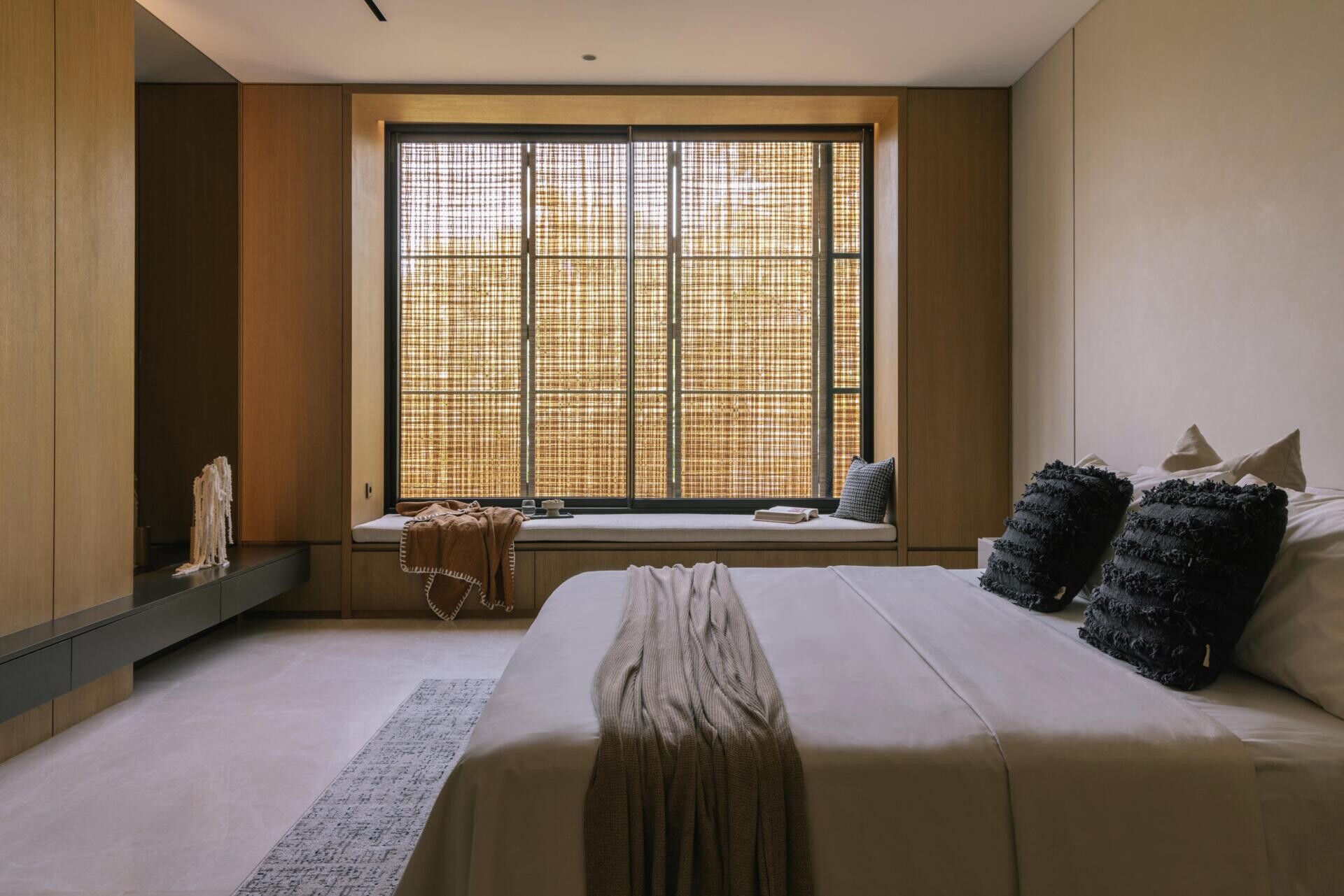 A modern primary bedroom with a built-in window bench, and a wood accent wall.