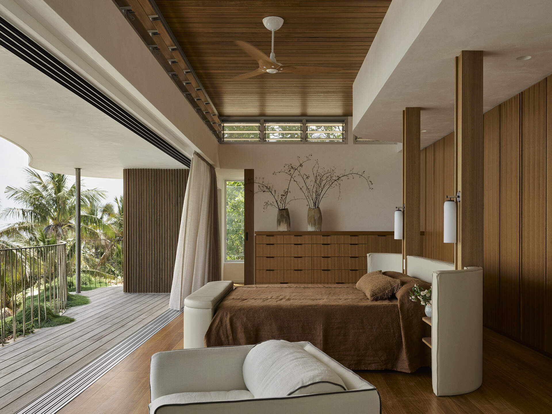Explore the elevated primary bedroom of this Byron Bay home, featuring warm timber, earthy finishes, mirrored surfaces and large openings that frame the expansive coastal outlook.