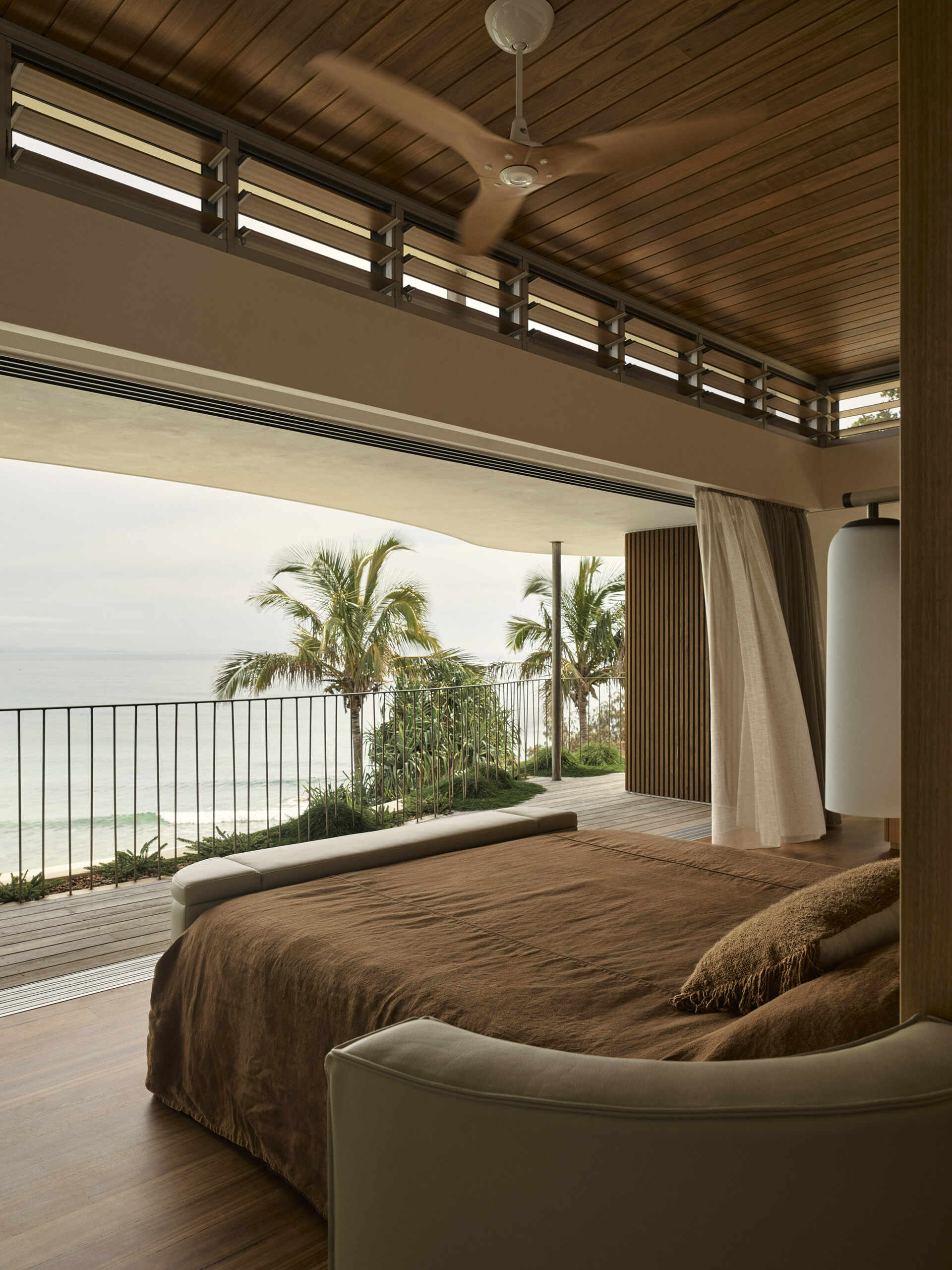 Explore the elevated primary bedroom of this Byron Bay home, featuring warm timber, earthy finishes, mirrored surfaces and large openings that frame the expansive coastal outlook.