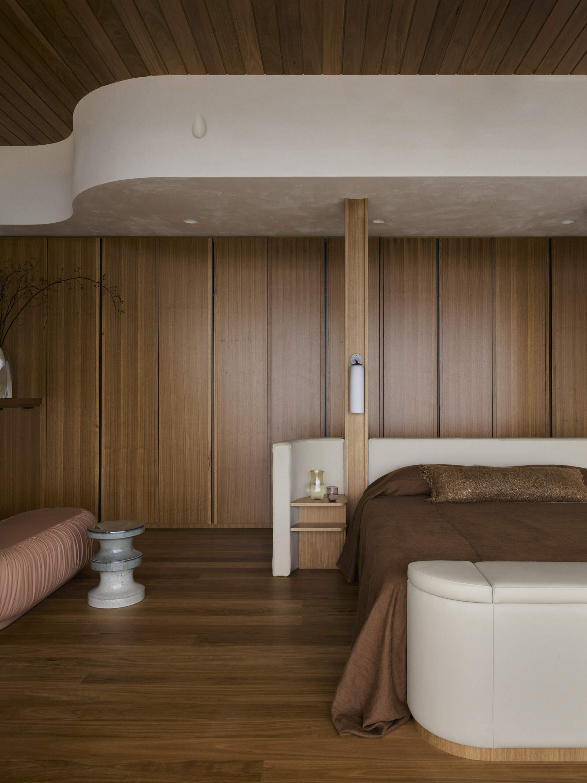 Explore the elevated primary bedroom of this Byron Bay home, featuring warm timber, earthy finishes, mirrored surfaces and large openings that frame the expansive coastal outlook.