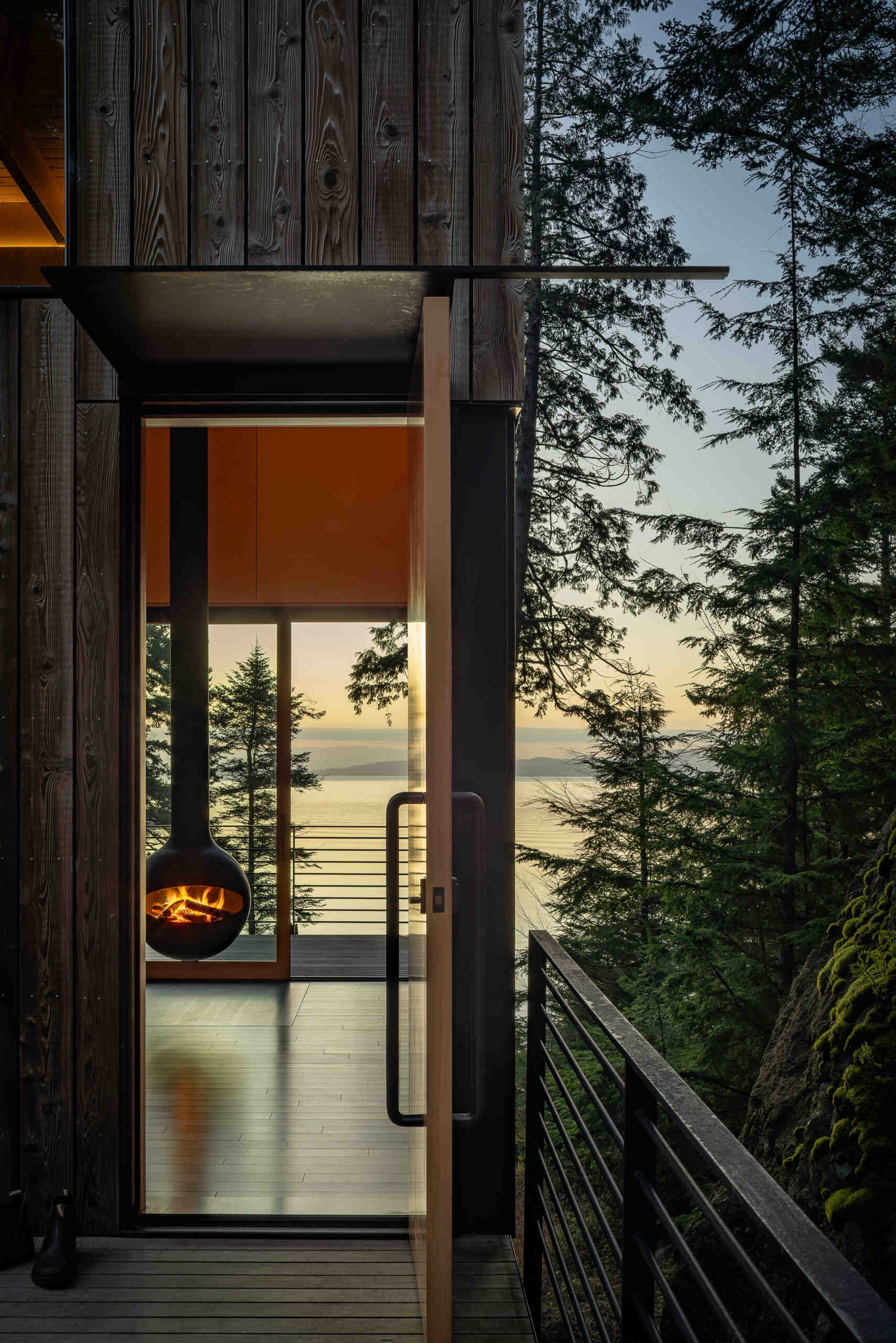 A suspended metal walkway winds through the forest to this tiny Blakely Island cabin, revealing views of Thatcher Bay before reaching the fir entry door.