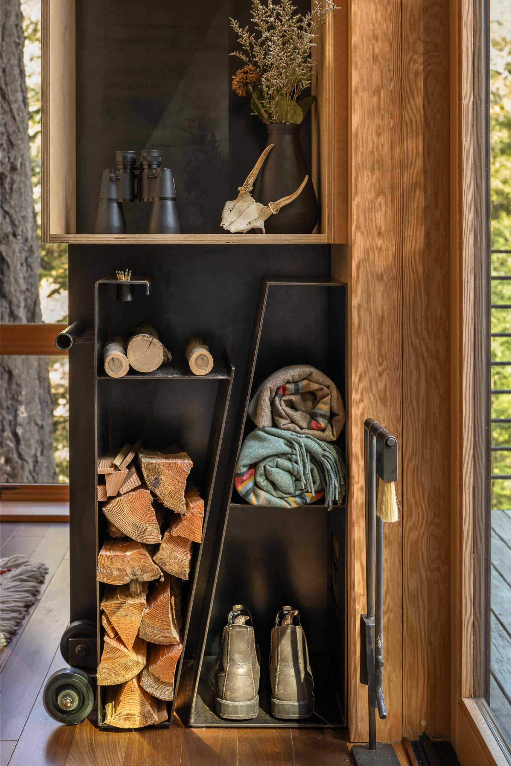 A custom steel fire cart and fireplace tools fit neatly into an angled storage nook in this 400-square-foot Blakely Island cabin by Wittman Estes.