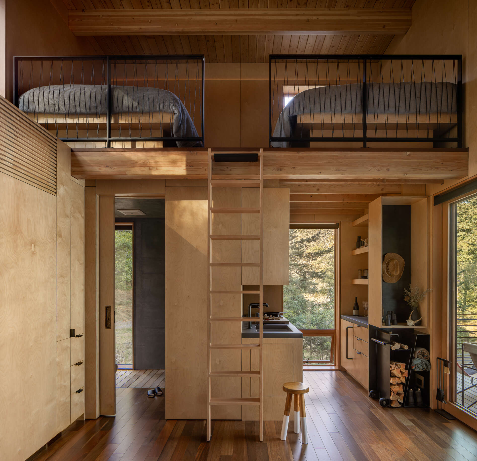 A custom maple ladder leads to a compact loft with two bunks above the kitchen, adding sleeping space without increasing the 400-square-foot cabin's footprint.
