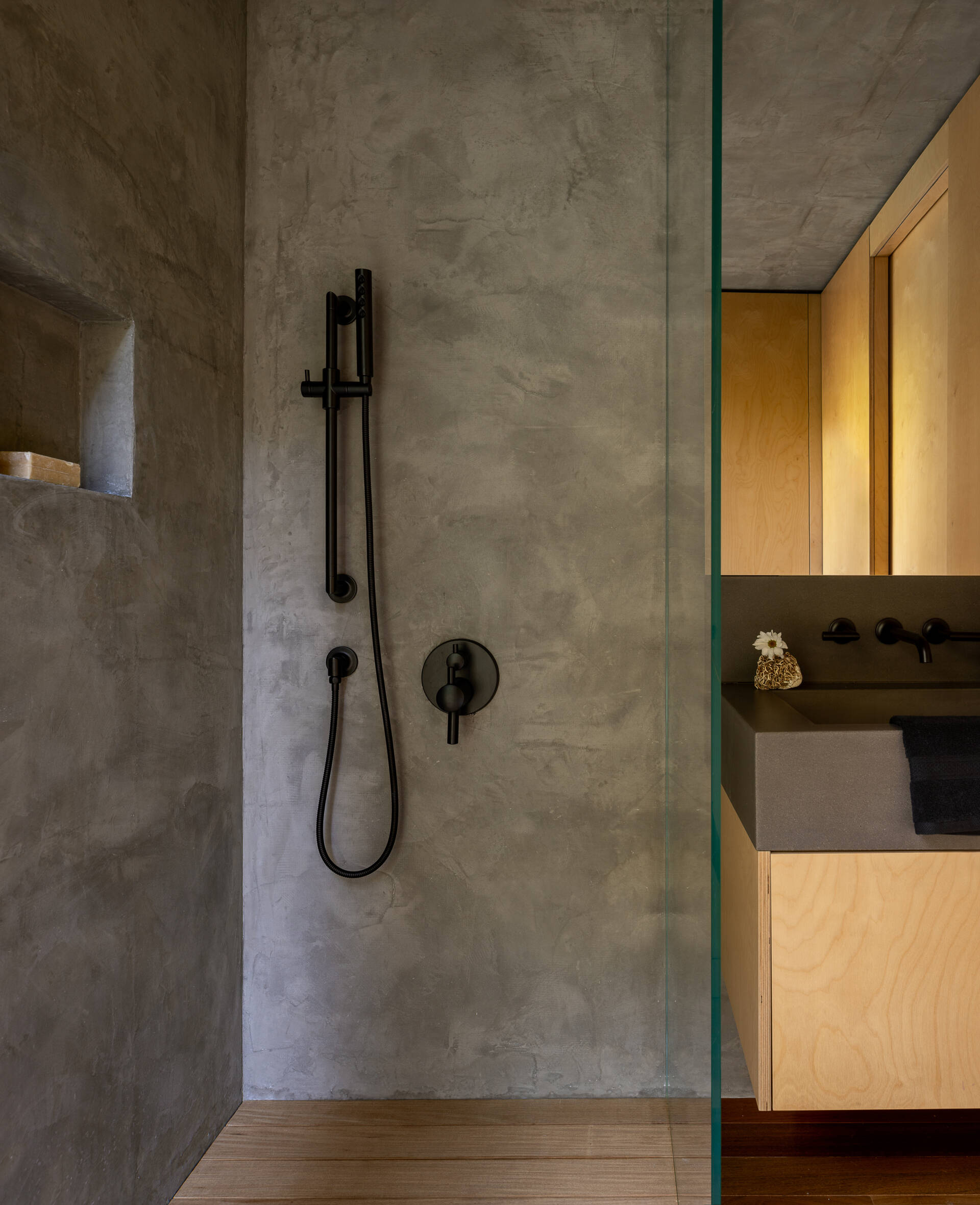 Tour the compact bathroom of the Blakely Island Cabin, featuring a glass-to-glass corner window overlooking the forest, concrete sink, microcement shower walls and matte black fixtures.