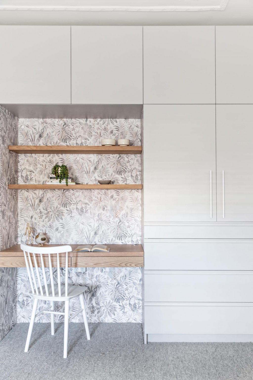 Find inspiration in this bedroom workspace, where a wood desk and shelving are surrounded by custom cabinetry and framed by botanical wallpaper.