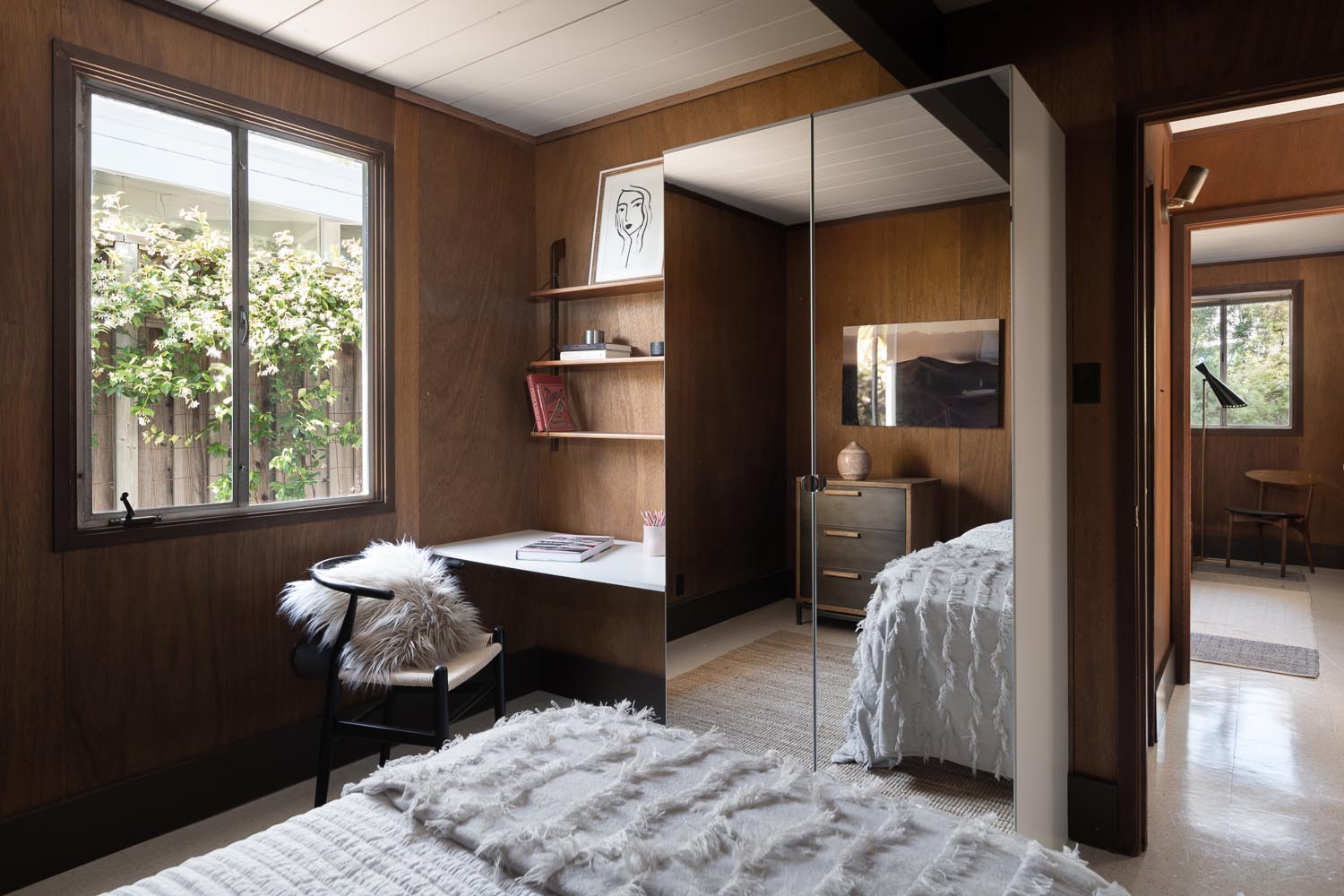 Step inside the bedrooms of this renovated Eichler house, featuring warm mahogany walls, mid-century furnishings, artwork and a custom desk with floating shelves.