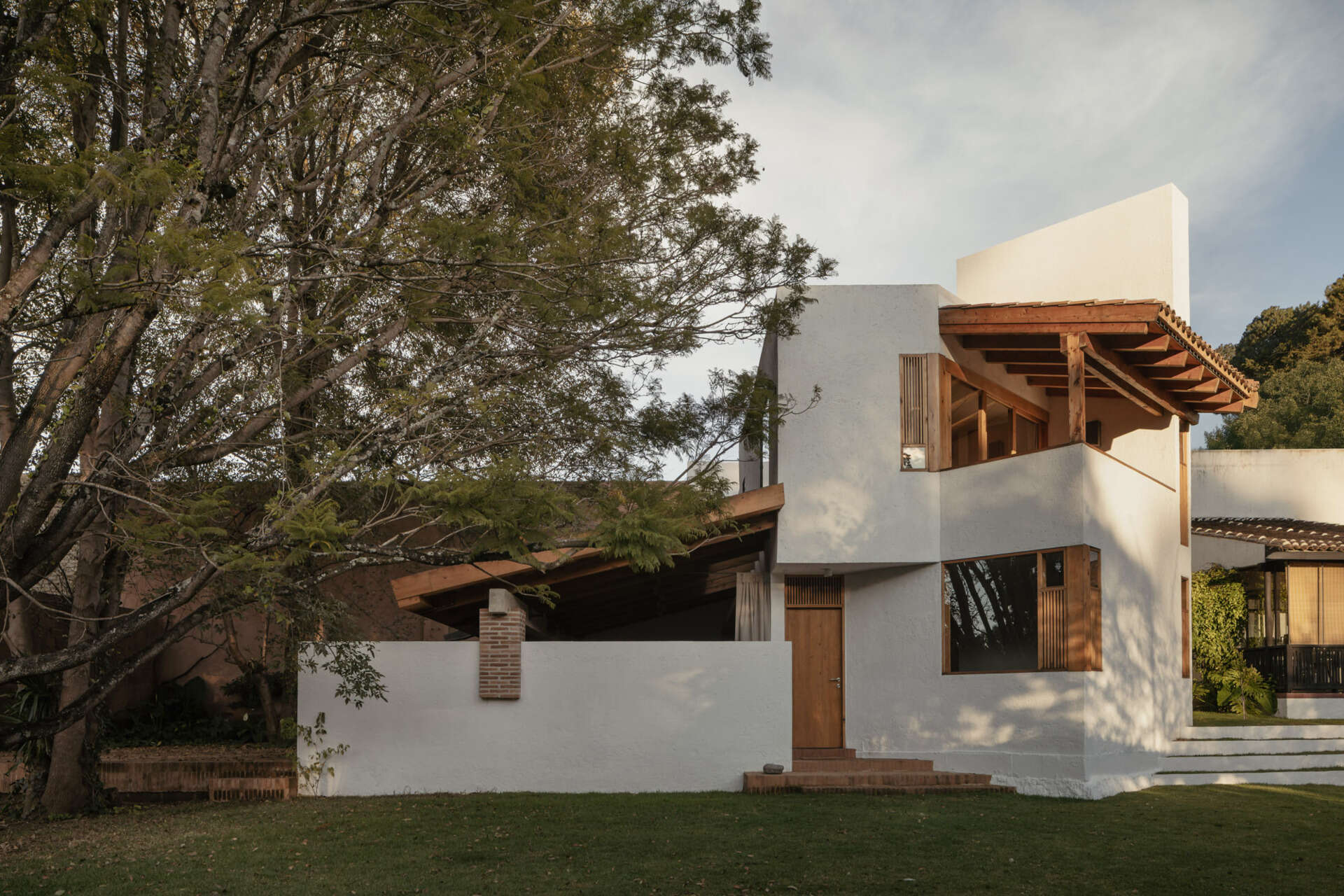 Explore the architecture of Casa Amona in Chiapas, México: textured white walls, timber-framed windows, a clay tile roof and a sheltered outdoor space beneath the trees.