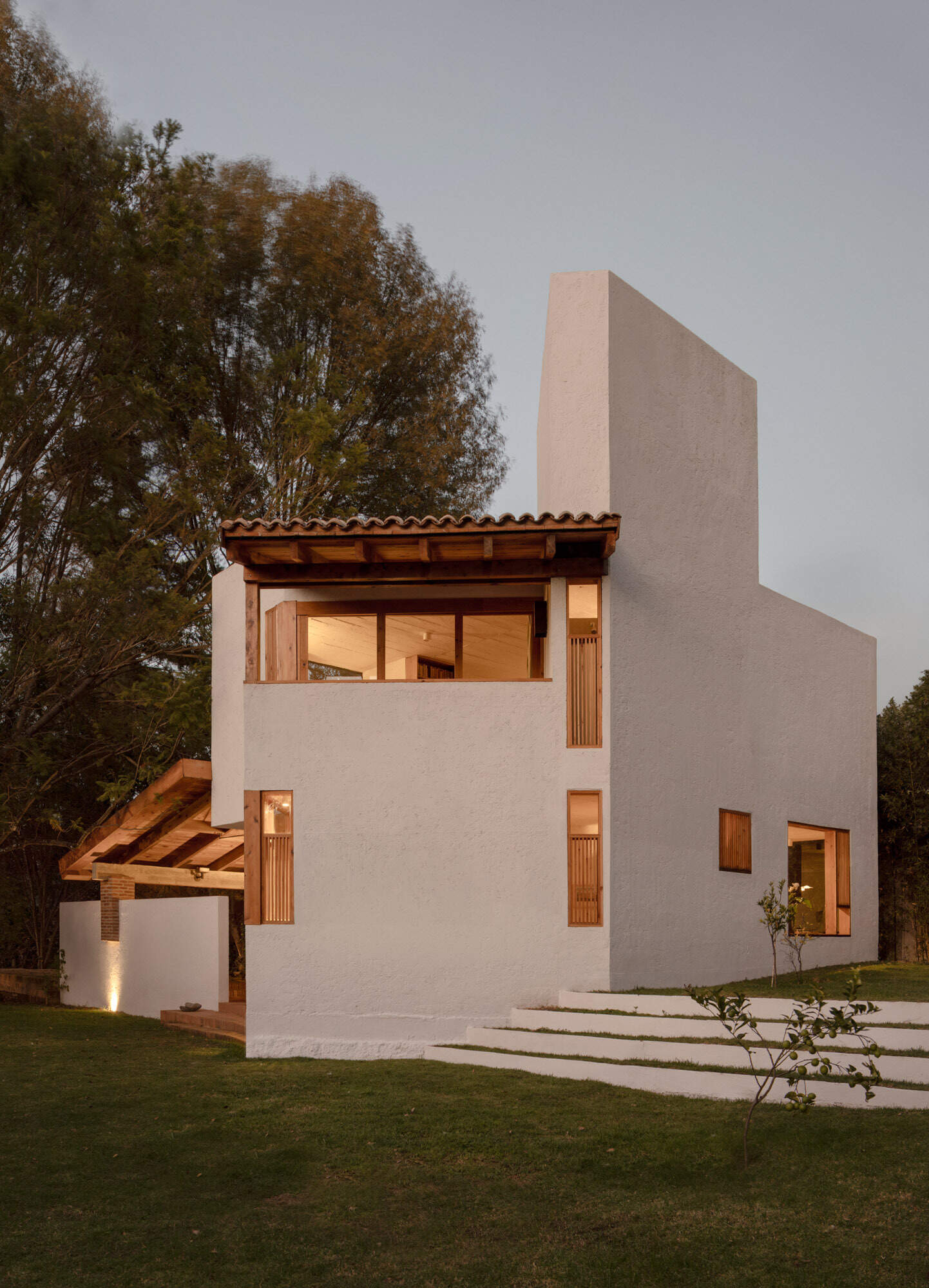 Explore the architecture of Casa Amona in Chiapas, México: textured white walls, timber-framed windows, a clay tile roof and a sheltered outdoor space beneath the trees.