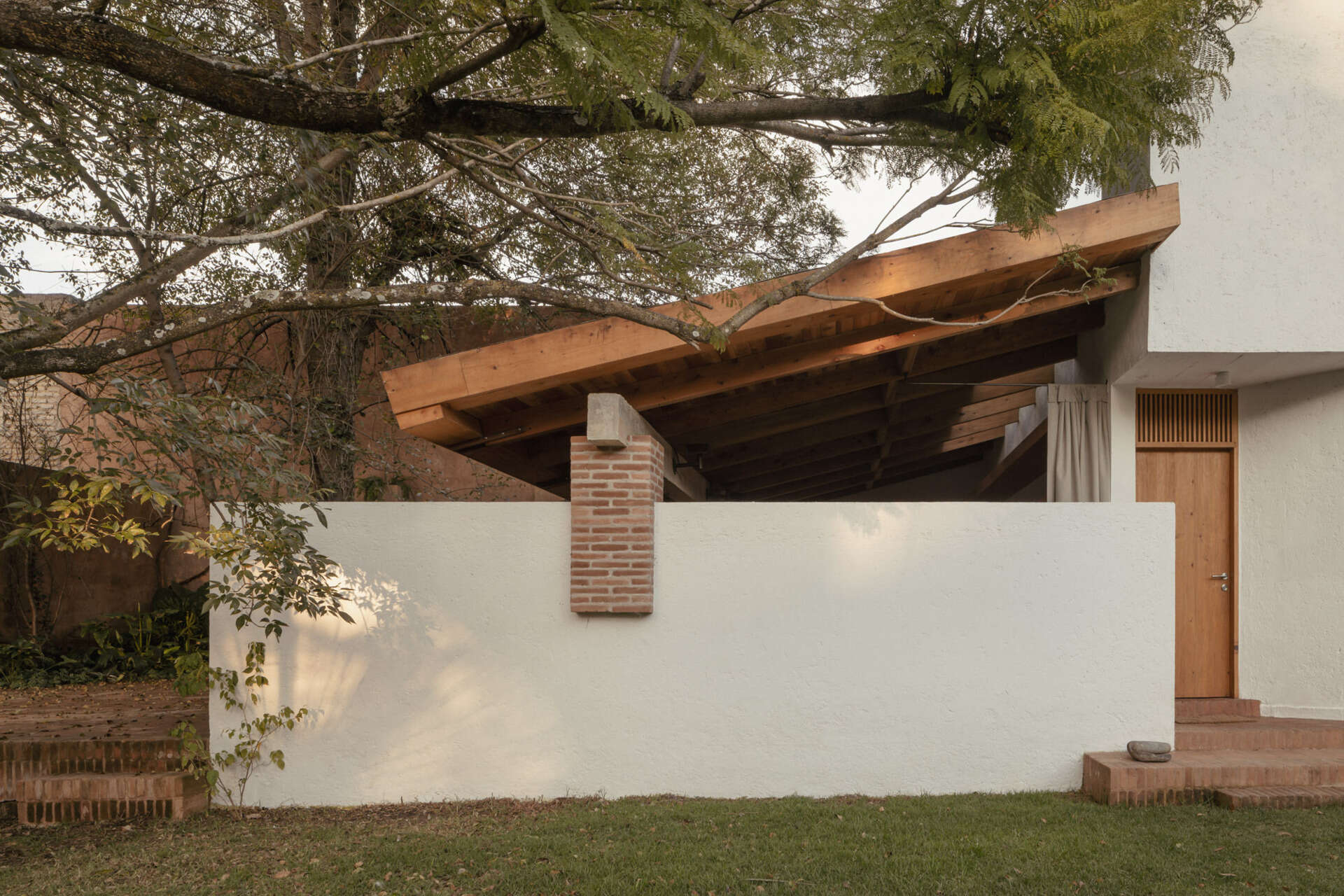 Explore the architecture of Casa Amona in Chiapas, México: textured white walls, timber-framed windows, a clay tile roof and a sheltered outdoor space beneath the trees.