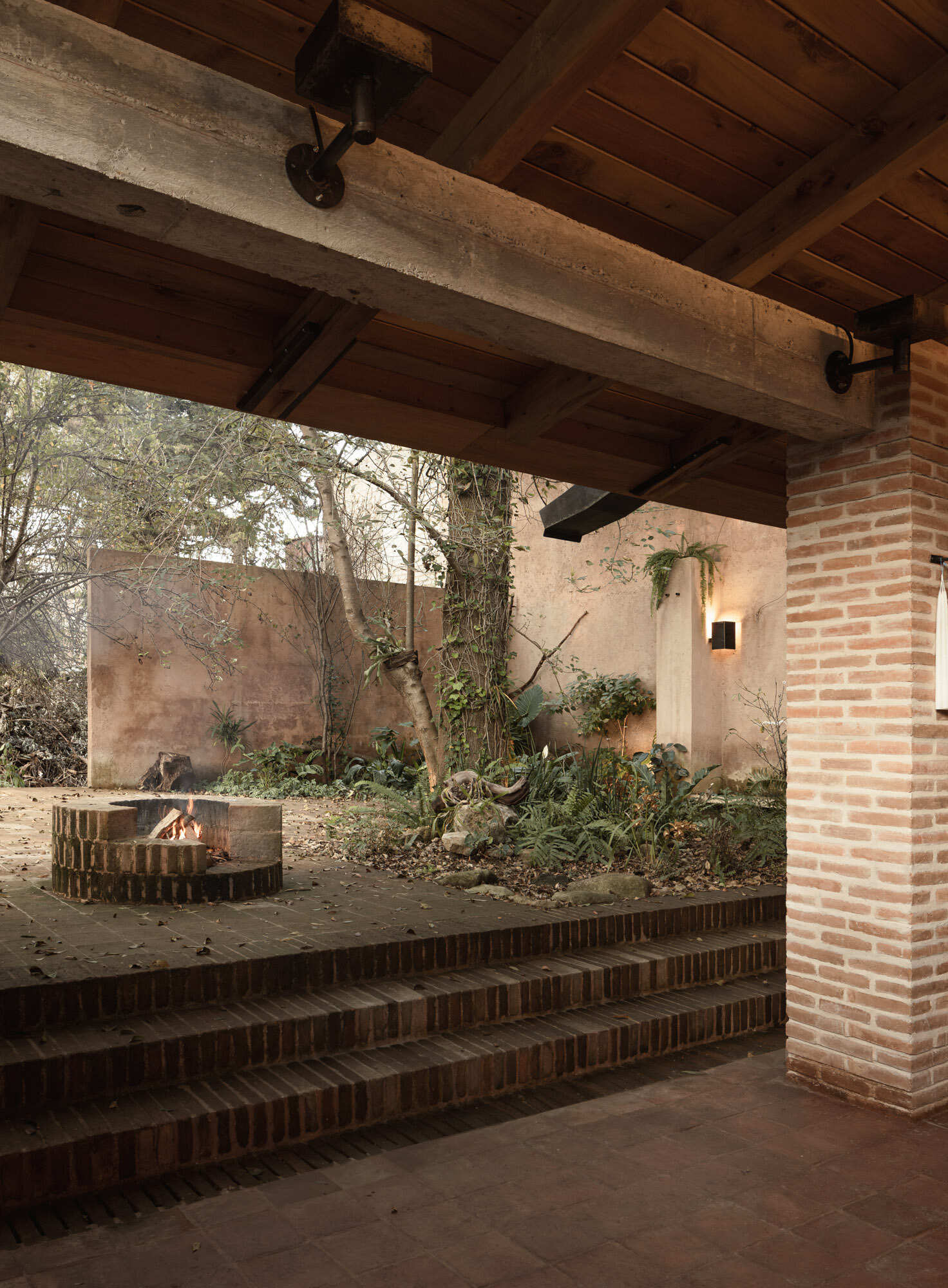 Step into Casa Amona’s courtyard in Chiapas, México, where an existing ash tree shades a brick fire pit and a covered workspace opens onto the planting.