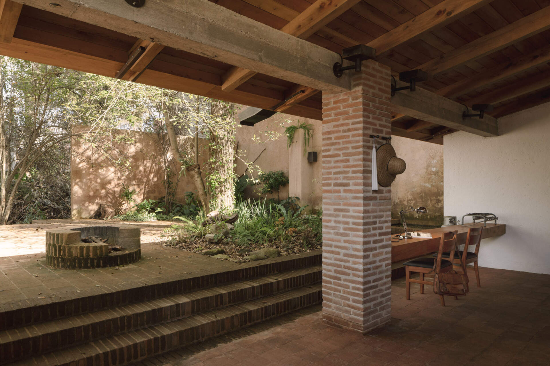 Step into Casa Amona’s courtyard in Chiapas, México, where an existing ash tree shades a brick fire pit and a covered workspace opens onto the planting.